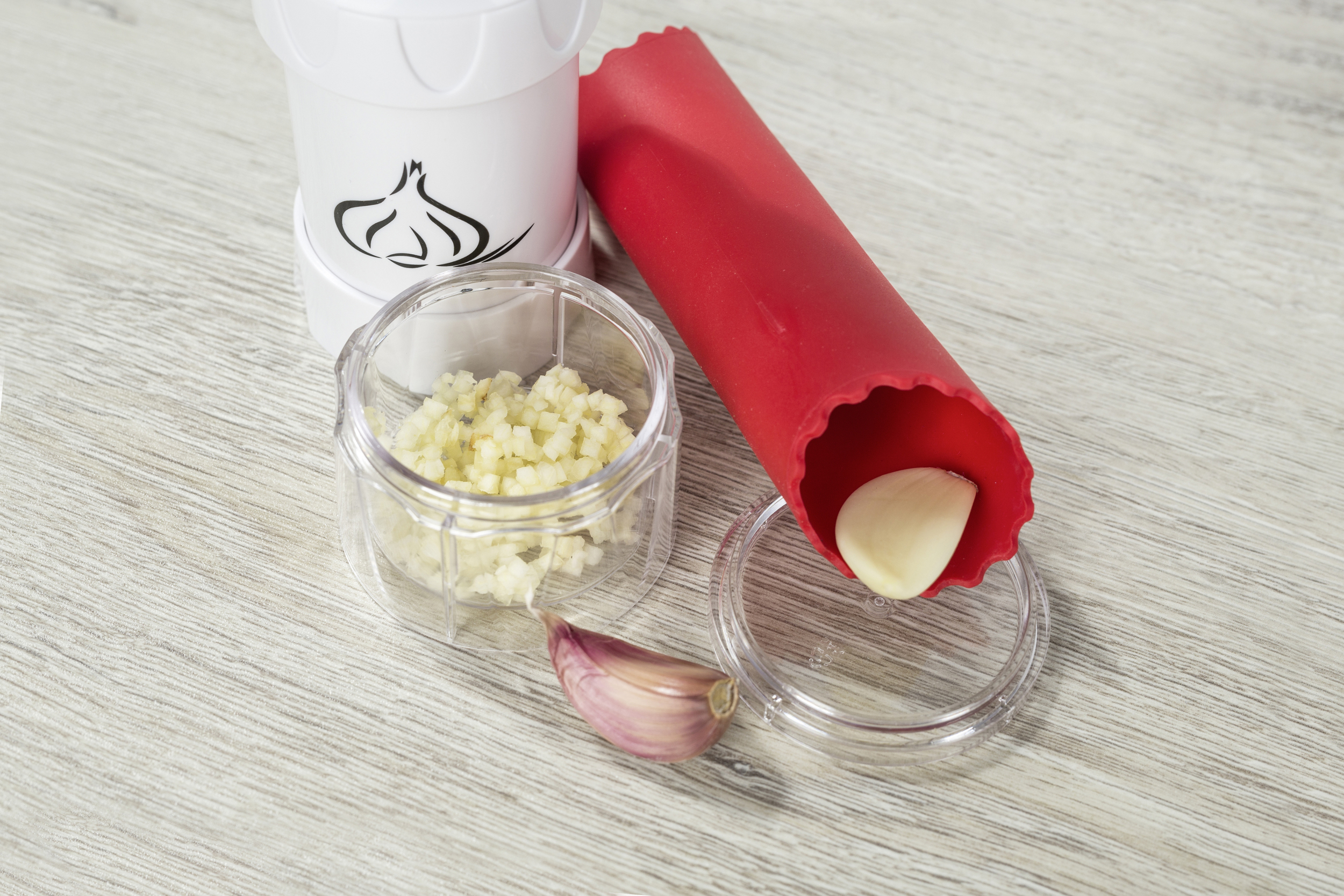 Knoblauchpresse und Zubehör: weiße Presse, kleiner Behälter mit gehacktem Knoblauch, rotes Rohr.