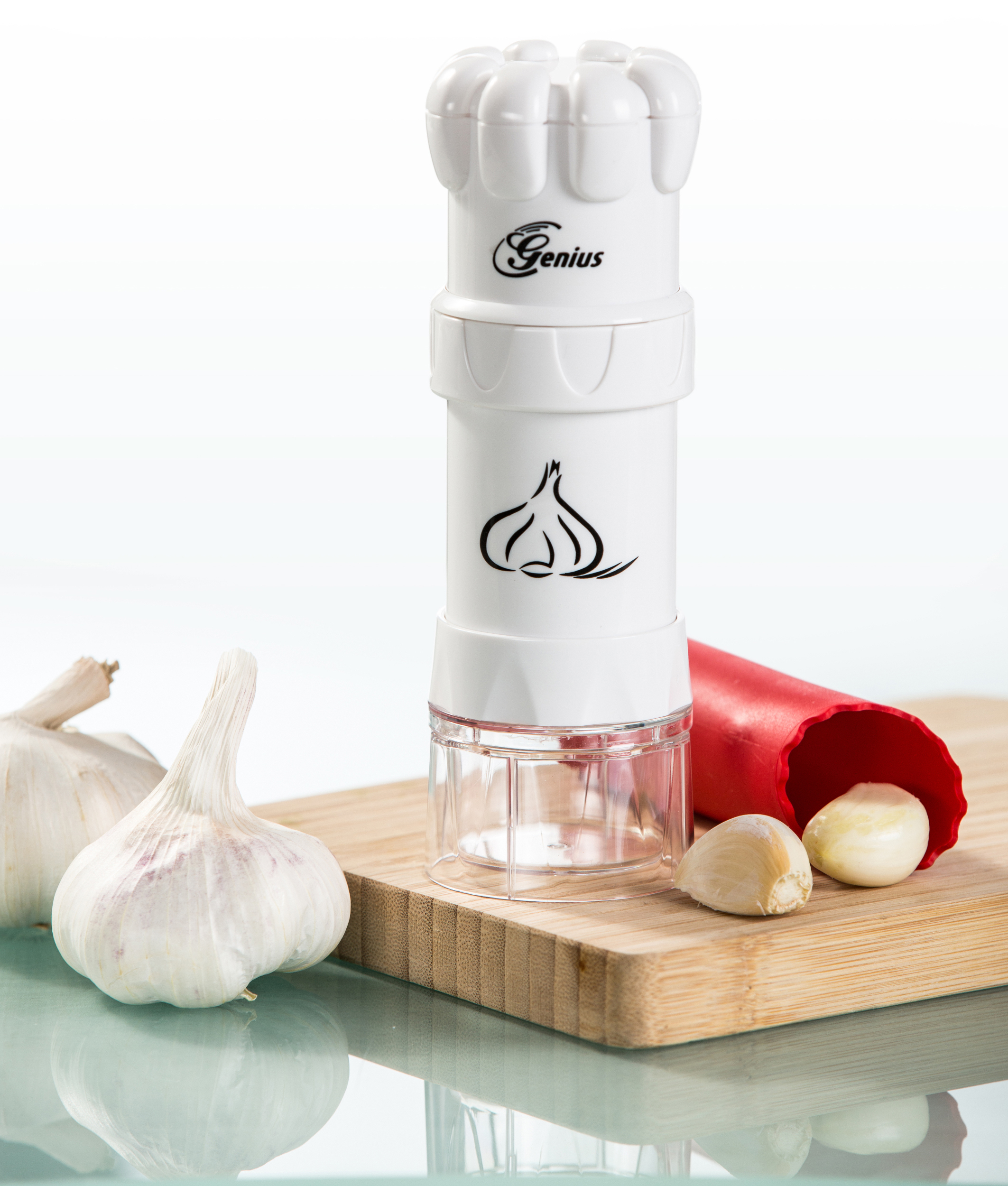 Weißer Knoblauchpresser mit Knoblauchzehen auf einem Holzbrett und ein roter Knoblauchschäler.