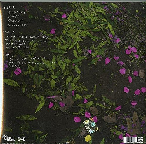 Achterkant albumhoes met tracklist op donkere ondergrond met verspreide groene bladeren en paarse bloemblaadjes.