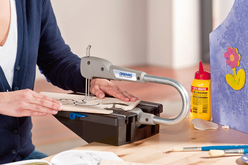 Személy Dremel Moto-Saw-t használ fán, sárga ragasztóval és lila háttérrel.