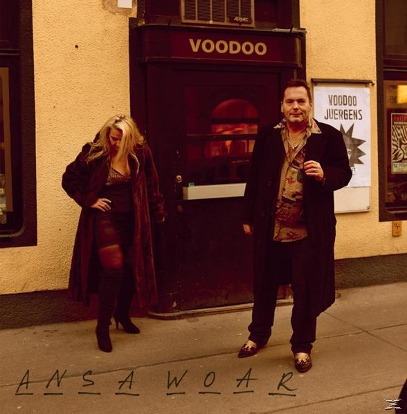 Mann und Frau stehen an einer Tür mit einem 'Voodoo'-Schild. Der Mann trägt einen Mantel, die Frau einen langen Mantel.