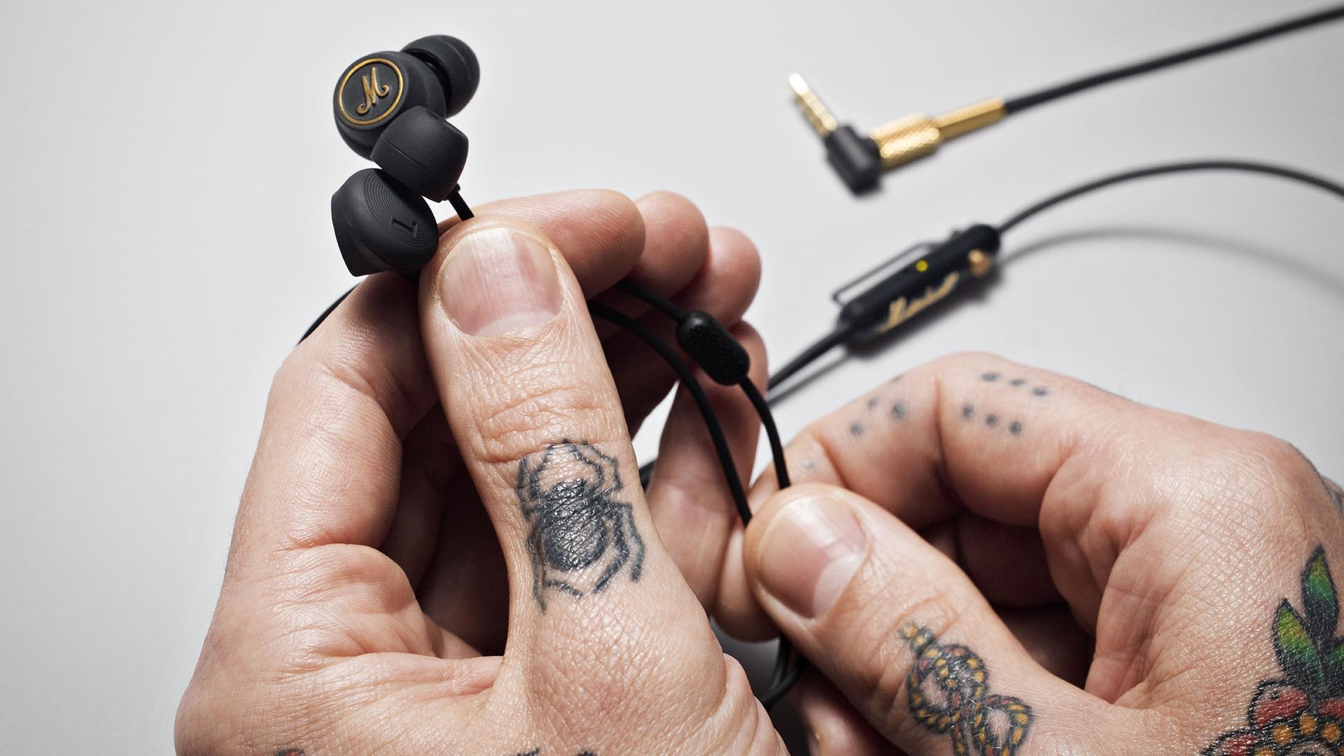 Mains tatouées tenant des écouteurs Marshall noirs avec des accents dorés.