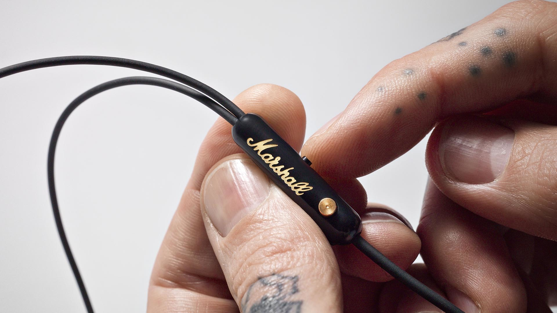 Gros plan d'une main tenant une commande d'écouteurs noire avec la marque 'Marshall'.