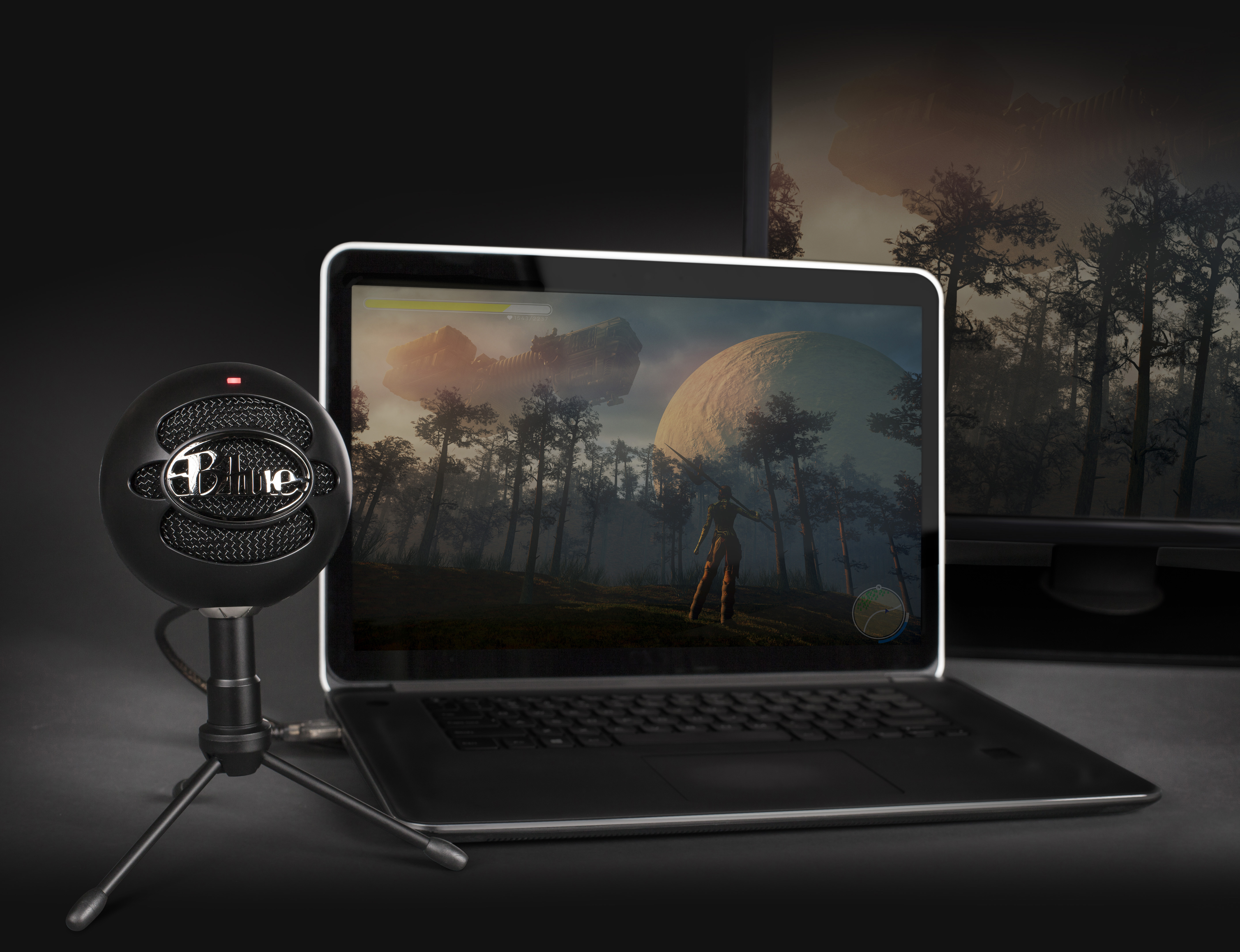 Ein schwarzes Mikrofon vor einem Laptop mit einer Spielszene auf dem Bildschirm.