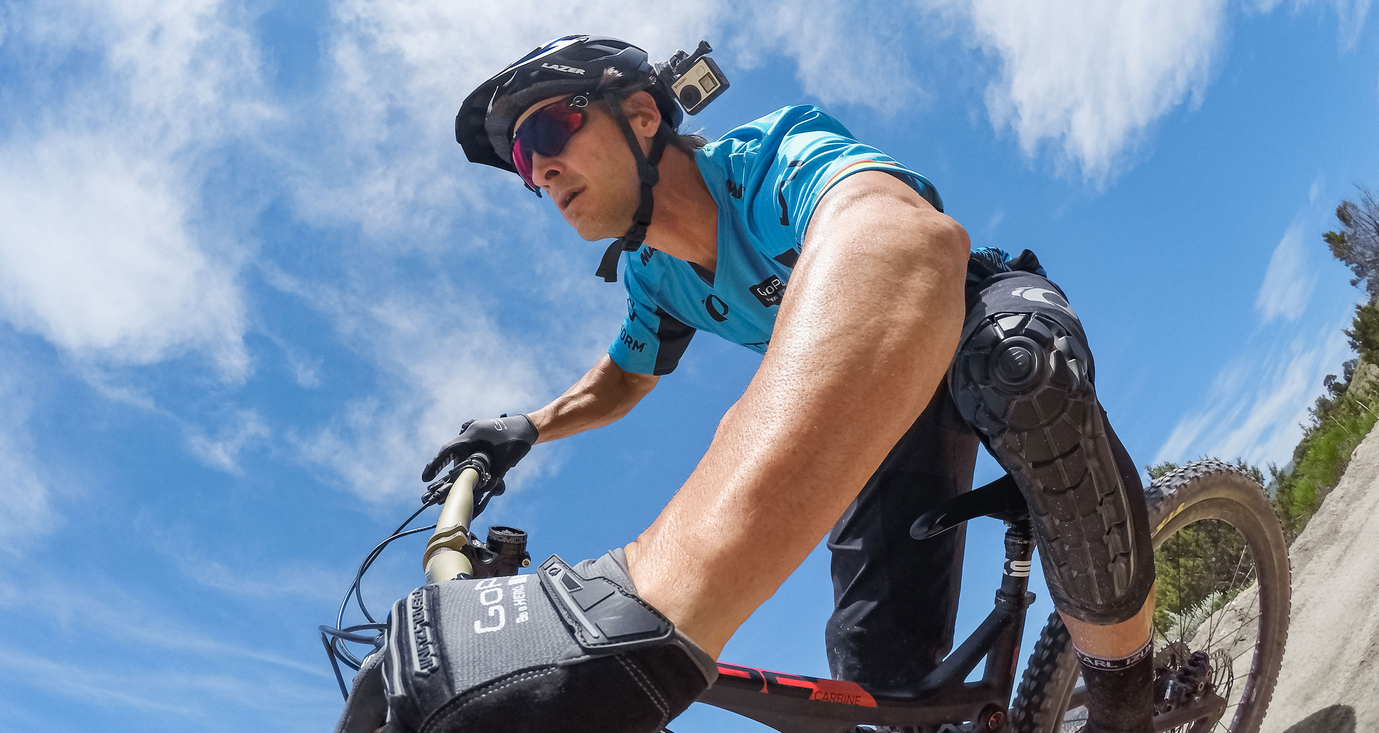 Mountainbiker mit Helm und Sonnenbrille fährt mit dem Fahrrad auf einer Dirt-Strecke.
