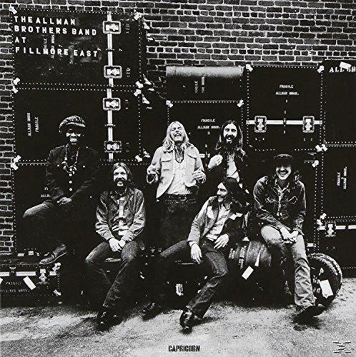Schwarz-Weiß-Foto einer Band. Männergruppe vor Kisten. Ziegelmauer im Hintergrund.