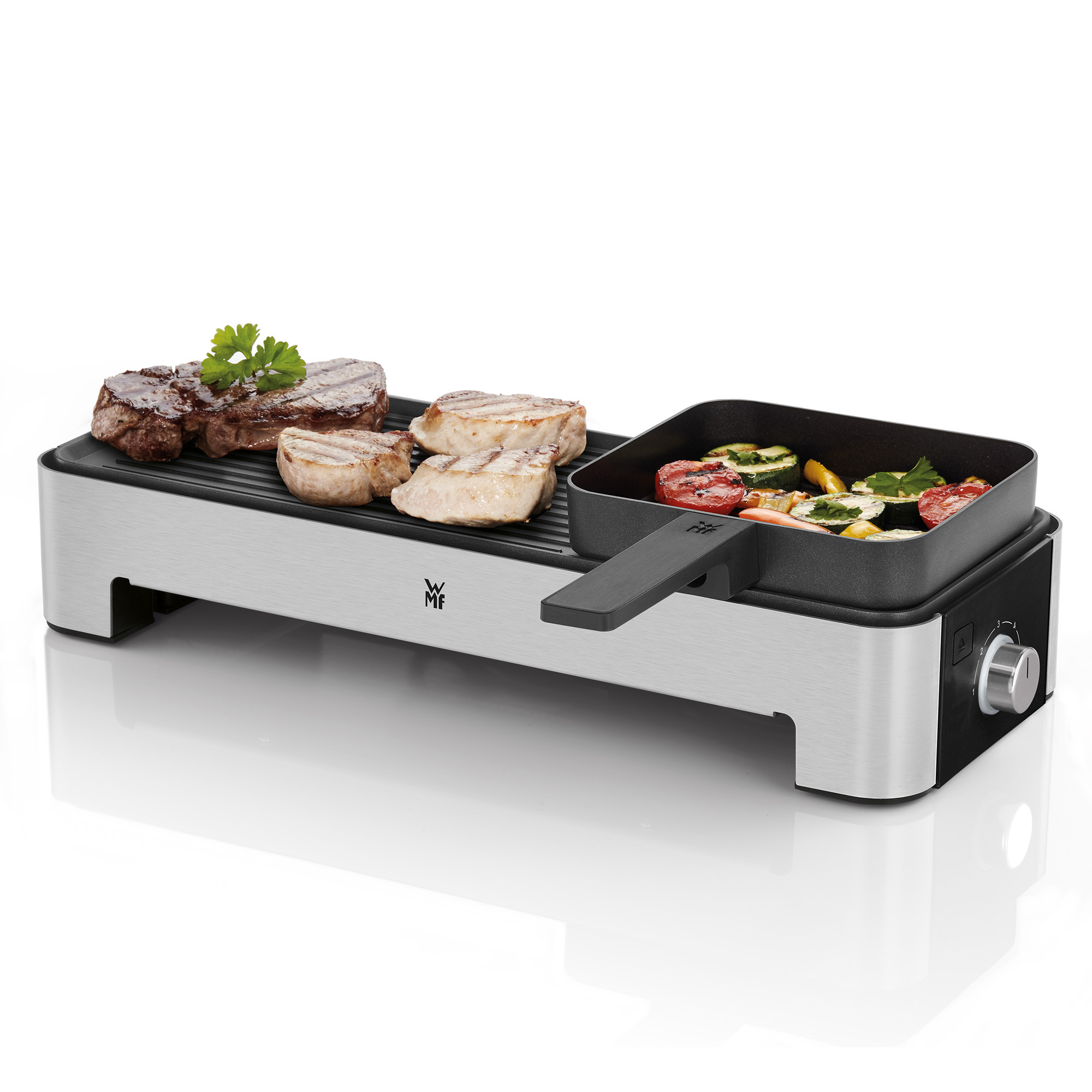 Grill avec des steaks et des légumes dans une poêle séparée, avec une poignée noire sur fond blanc.