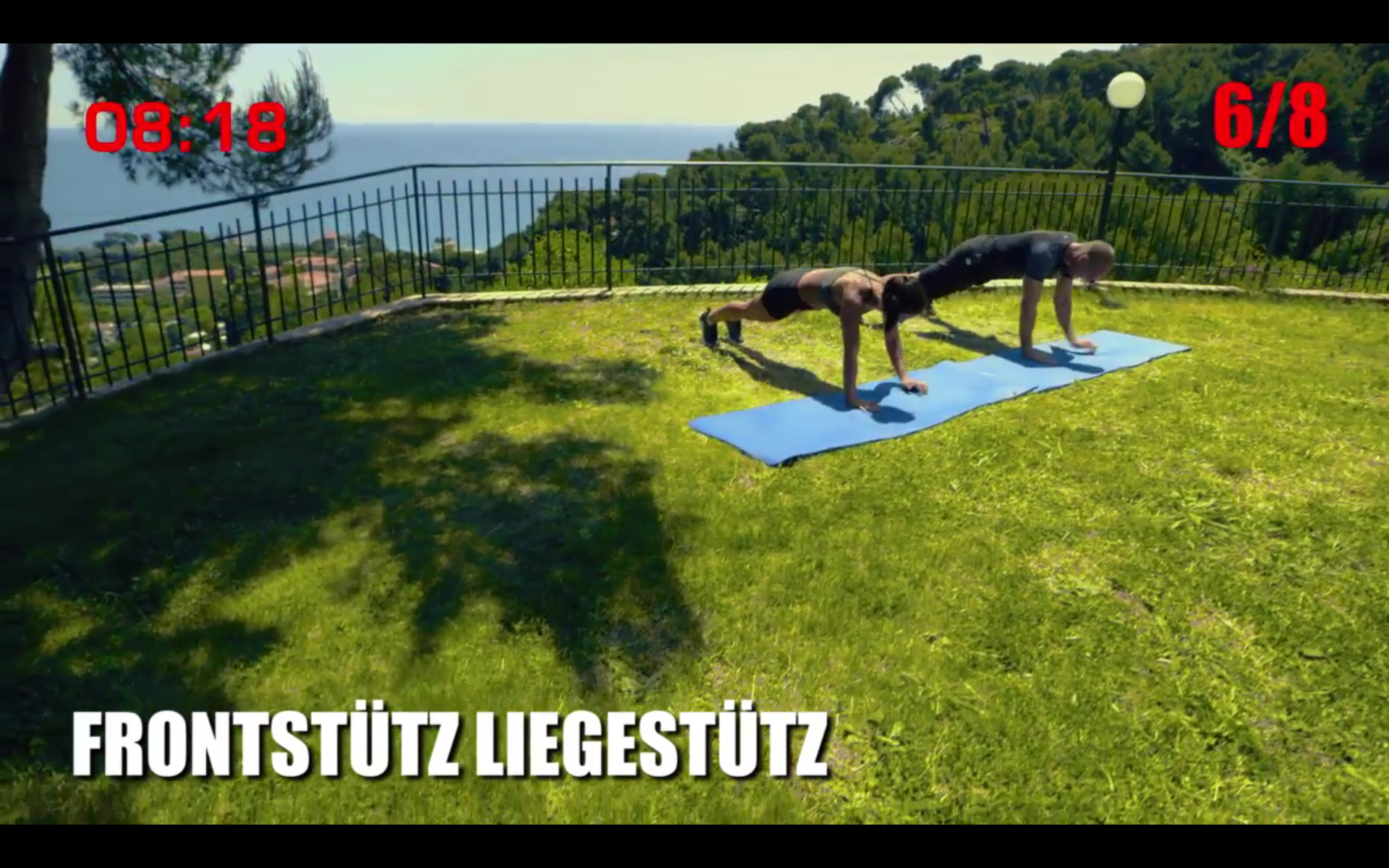 Zwei Männer machen Liegestütze auf einer blauen Matte, grünes Gras, Bäume und Zeit/Satz-Nummern.