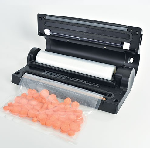 Een zwarte vacuümmachine met een rol plastic en een zakje gesneden wortels.