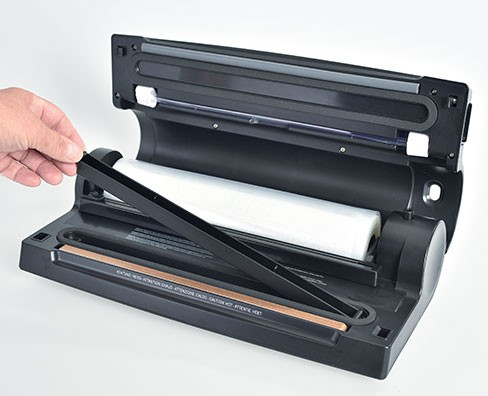 Vacuümmachine met een rol plastic erin. Een hand gebruikt het.