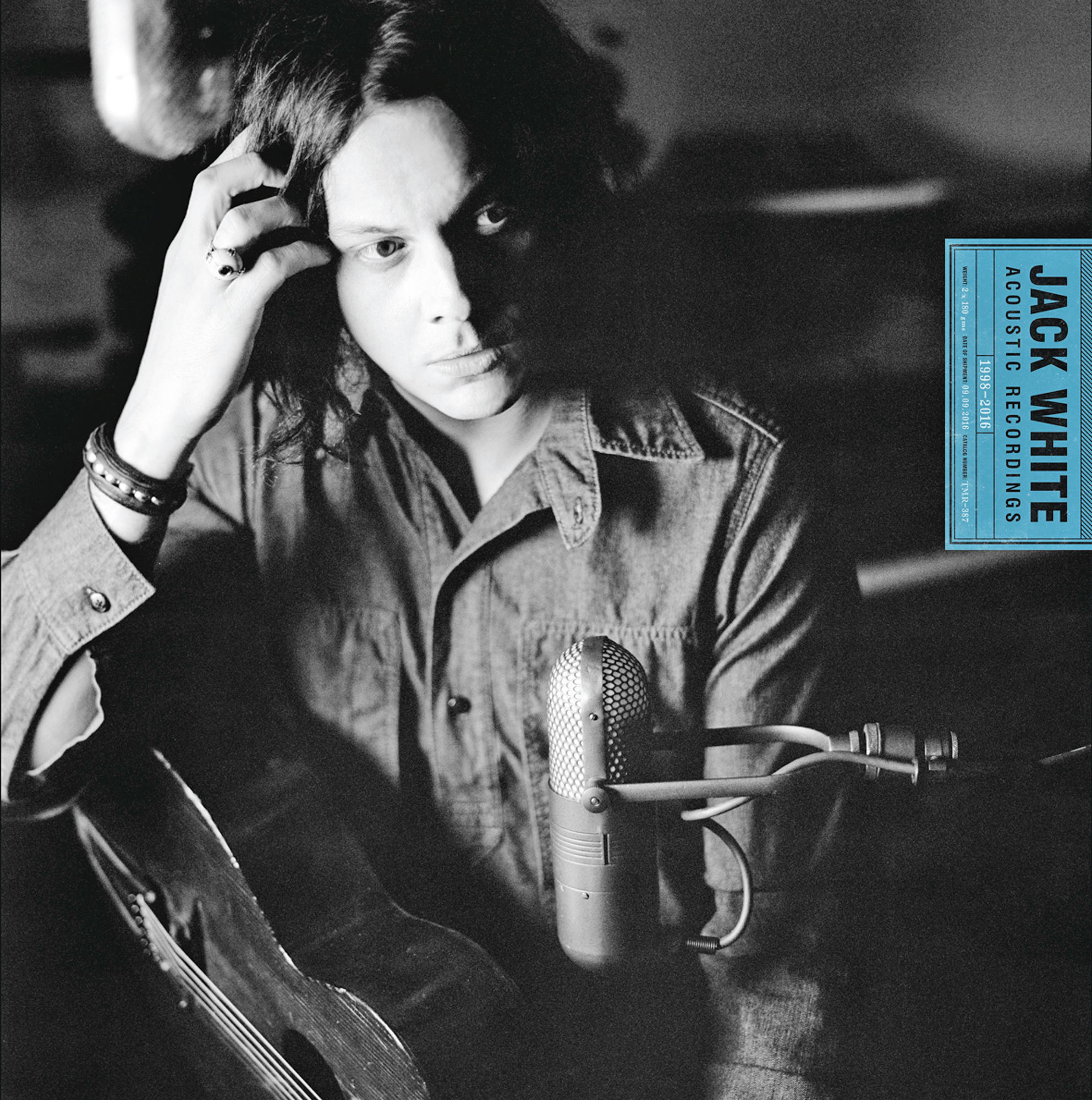 Jack White in zwart-wit. Hij houdt zijn hoofd vast met zijn hand, heeft een microfoon en een gitaar links.