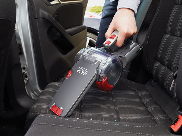 Kéz porszívózza az autósülést egy fekete-piros Black+Decker porszívóval.