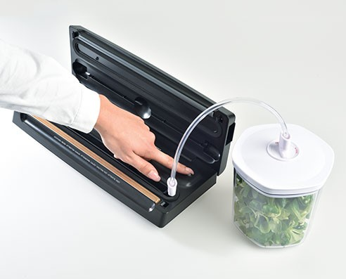 Une personne utilisant une scelleuse alimentaire avec un récipient de verdure et un tuyau d'aspiration connecté.