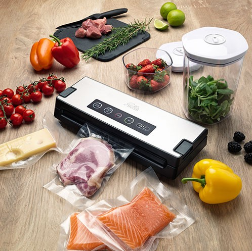 Une table avec divers ingrédients : viande, légumes, fraises et une machine à emballer sous vide.