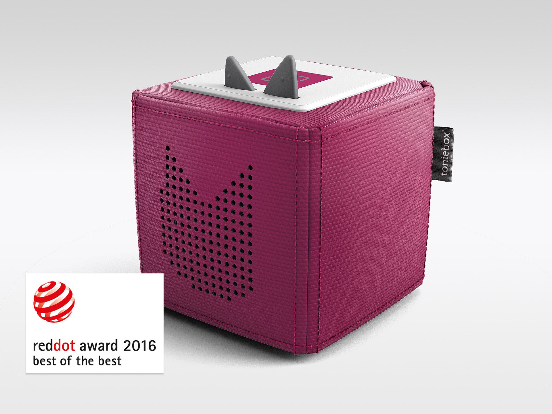 Eine magenta Toniebox mit zwei grauen Ohren oben, einem weißen Deckel und einem Lautsprecher. Es ist ein Red Dot Award-Gewinner.