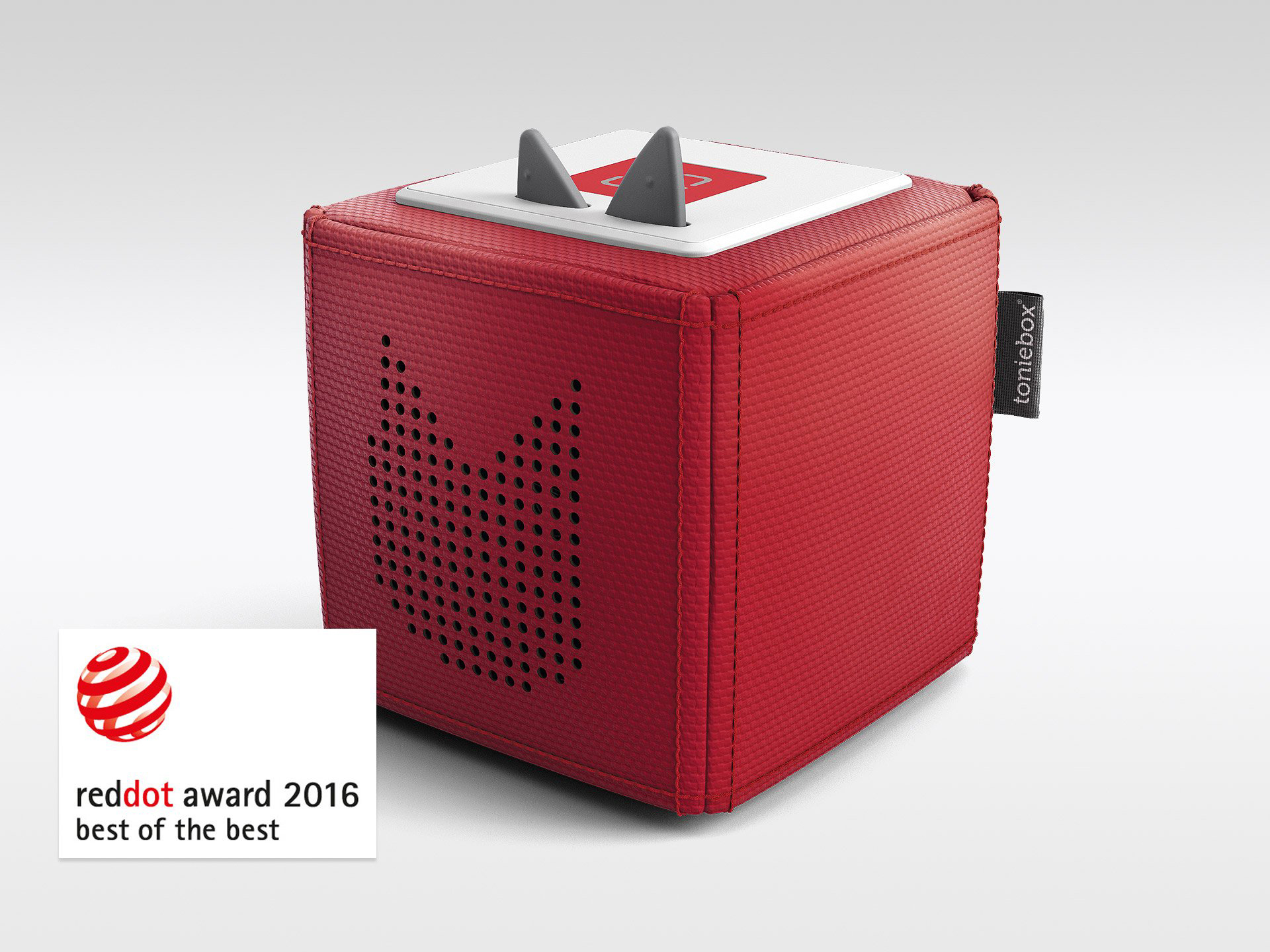 Roter Toniebox-Lautsprecher. Hat zwei graue Ohren oben. Reddot-Award-Logo unten links.