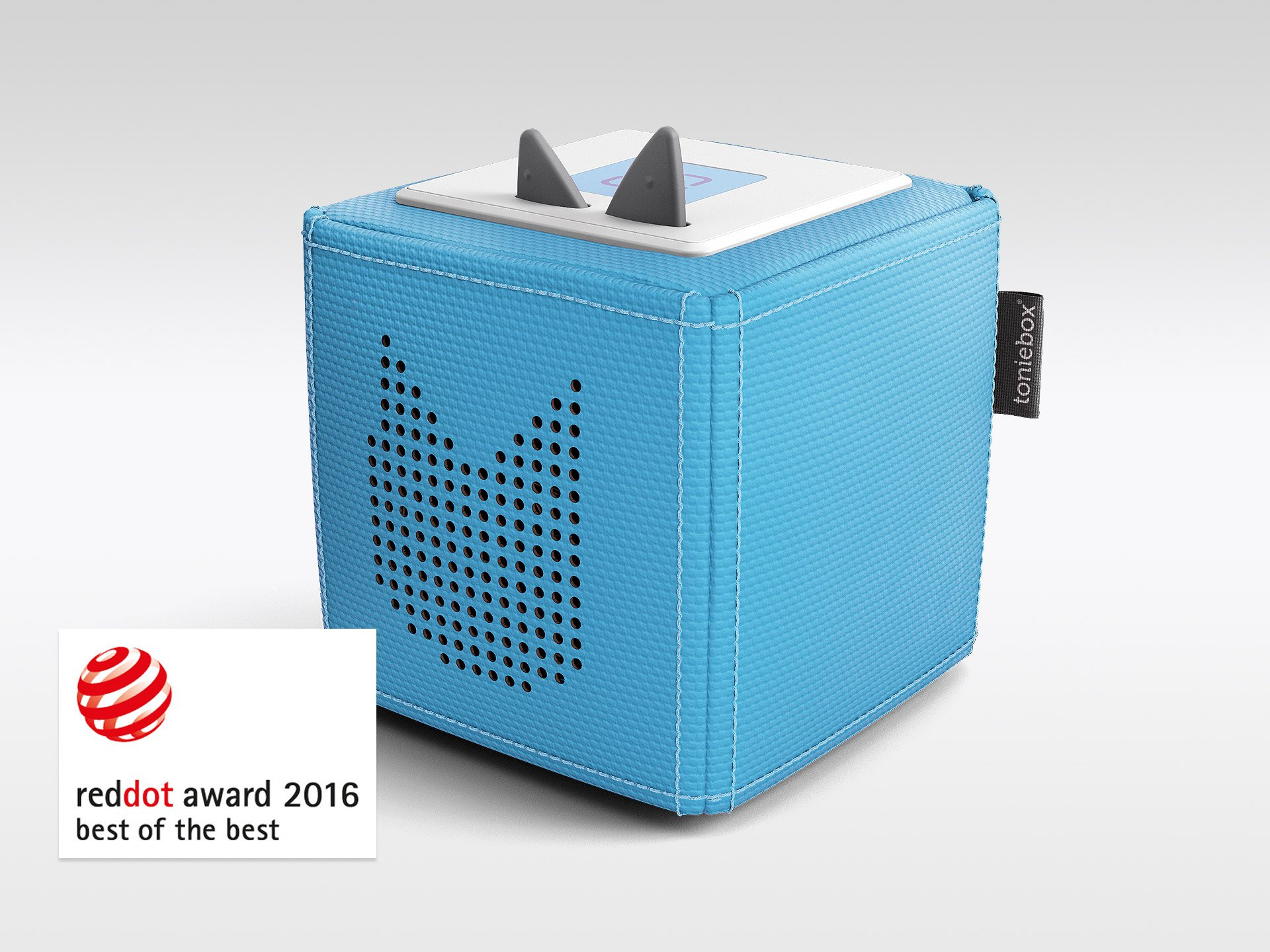 Ein blaues, würfelförmiges Gerät mit grauen Ohren oben. Es hat ein Logo und ein rotes Punkt-Award-Abzeichen.