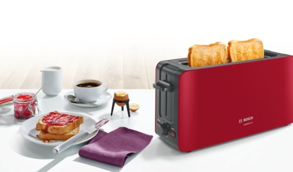 Ein roter Toaster mit zwei Scheiben Toastbrot. Weißer Tisch, Frühstücksszene.