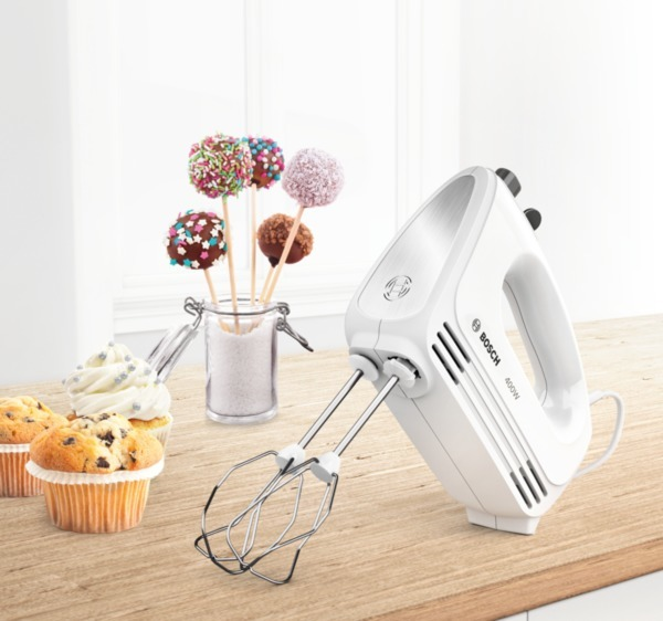 Ein weißer Handmixer mit einem Holztisch und Cupcakes und Cake Pops.