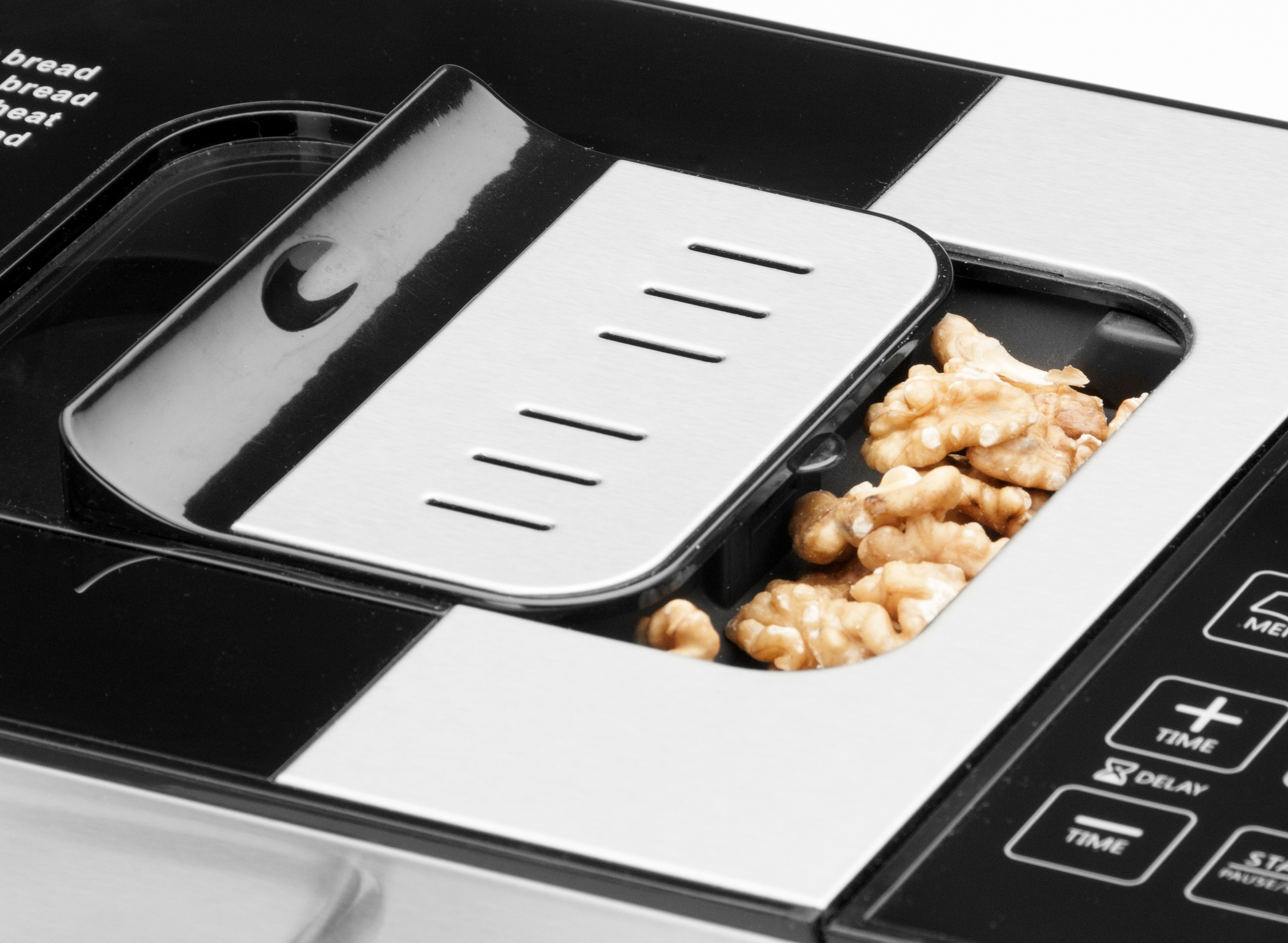 Nahaufnahme eines Brotbackautomaten mit offenem Deckel, der Walnüsse zeigt. Schwarzes und silbernes Design.