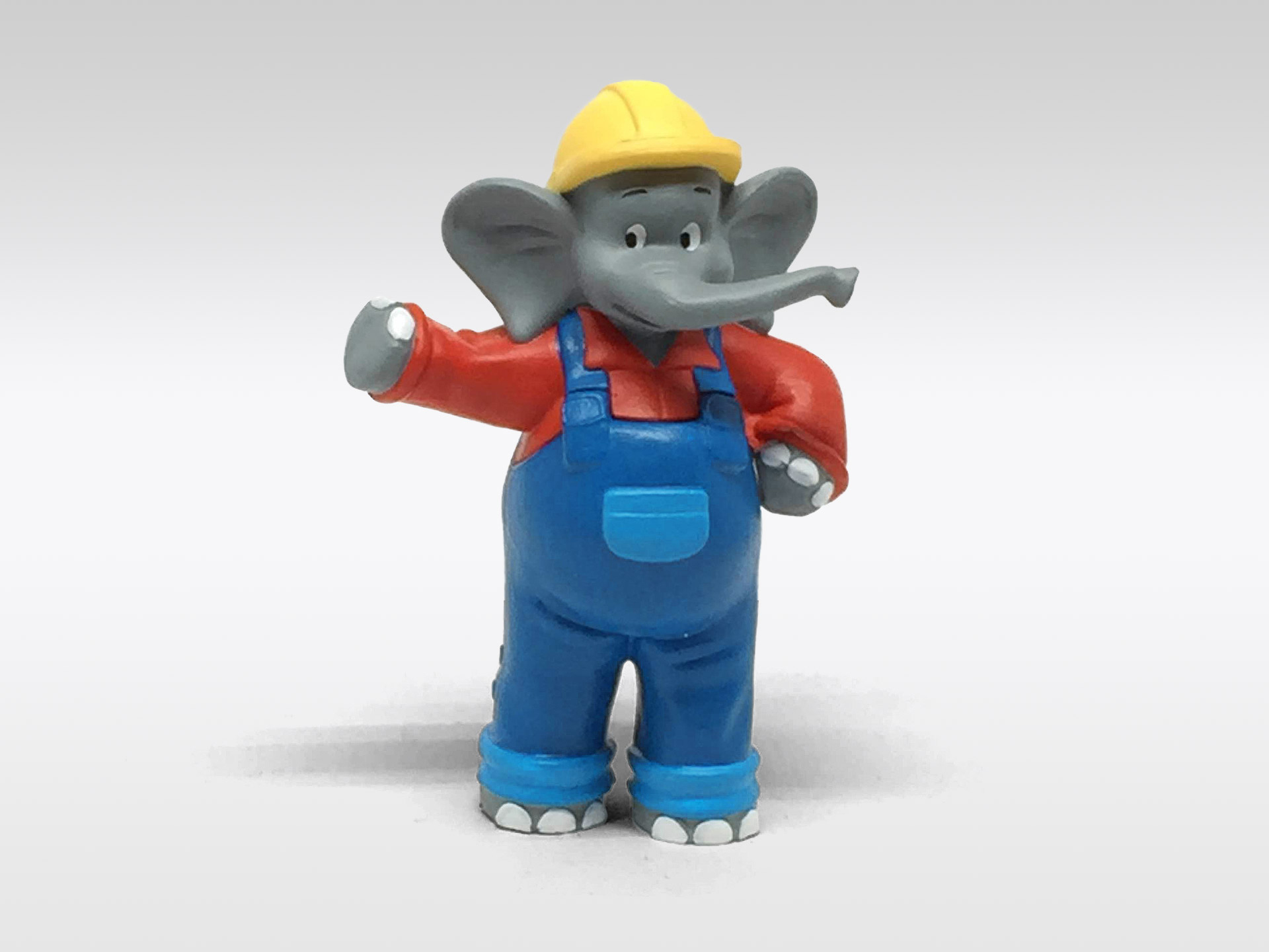 Eine Elefantenfigur mit gelbem Helm und Latzhose steht auf weißem Untergrund.