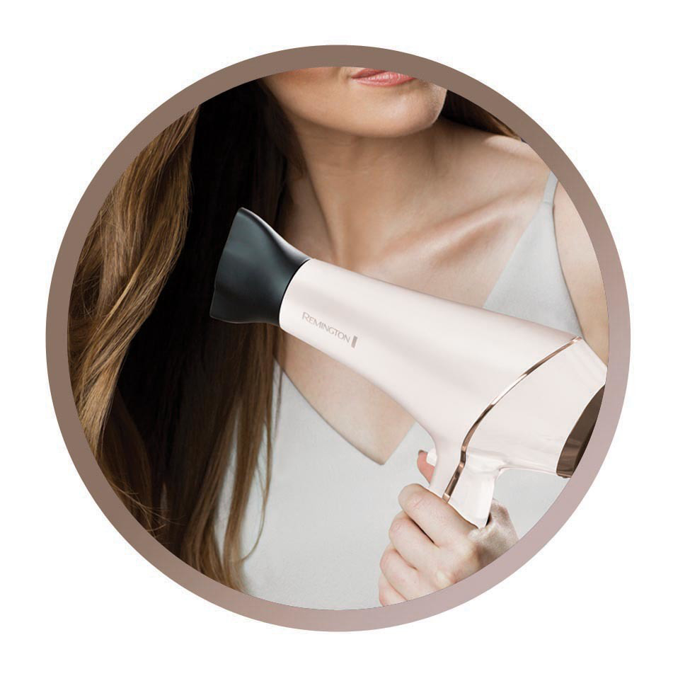 Une femme tenant un sèche-cheveux blanc et doré.