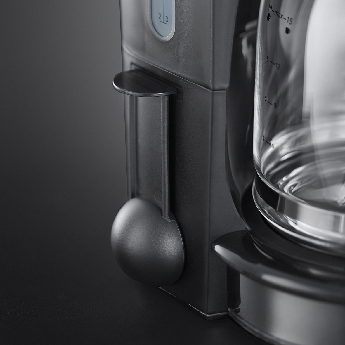 Nahaufnahme einer Kaffeemaschine. Dunkelgraues Gehäuse, Wasserstandsanzeigen und eine transparente Glaskaraffe.