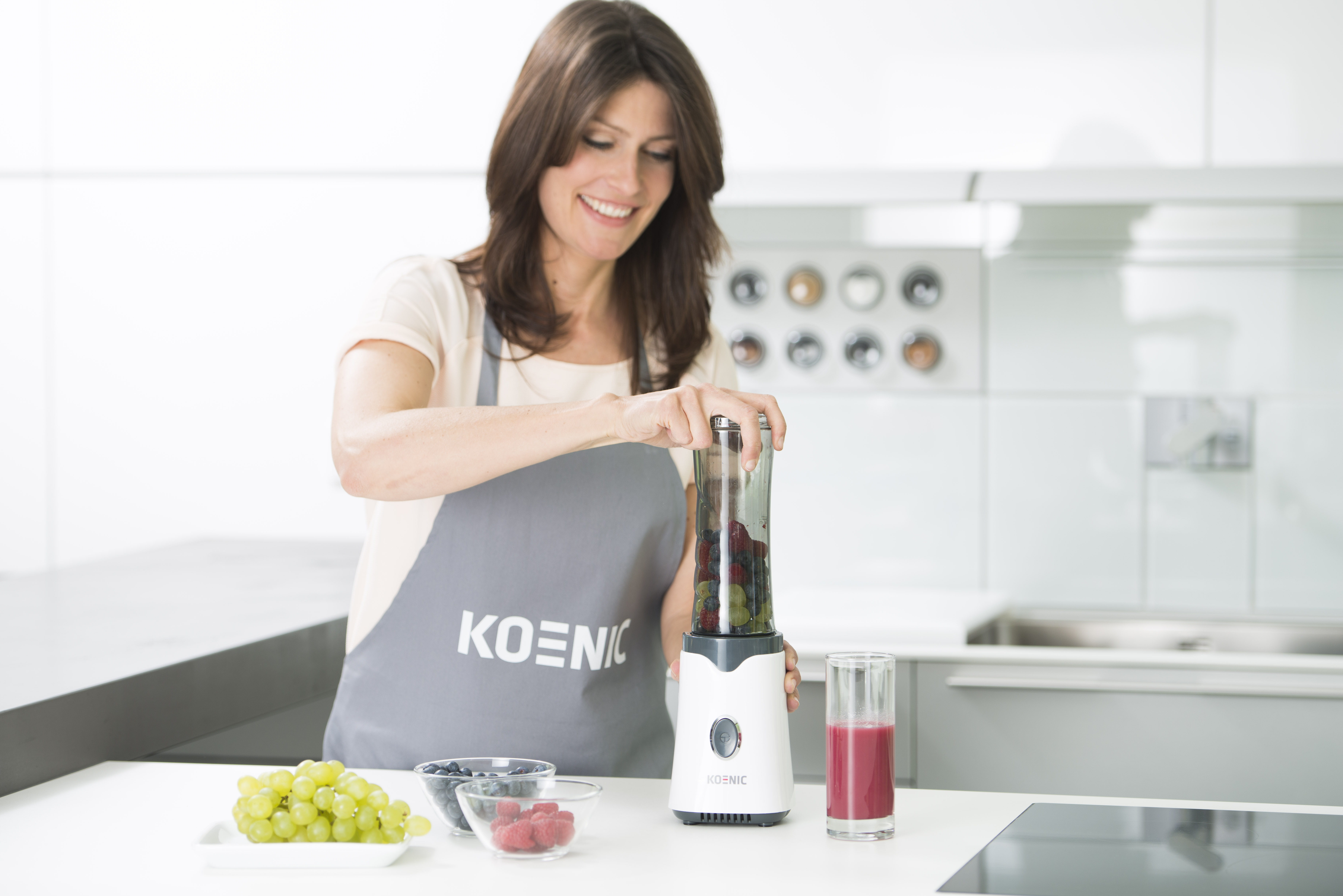 Eine Frau macht einen Smoothie. Früchte und Mixer stehen auf der Theke. Küchenumgebung.