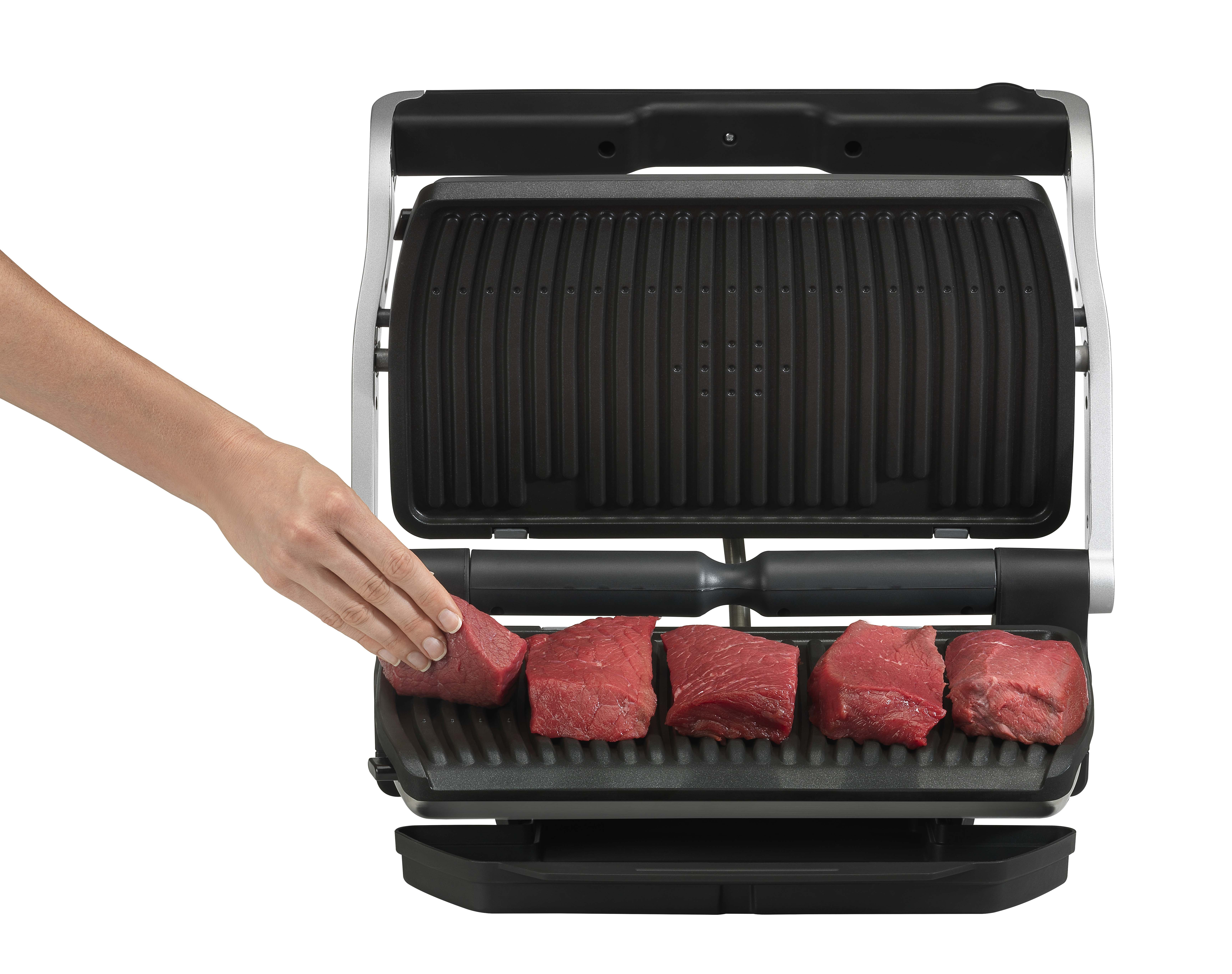 Een persoon plaatst rauw vlees op een zwarte grill. De grill staat open.