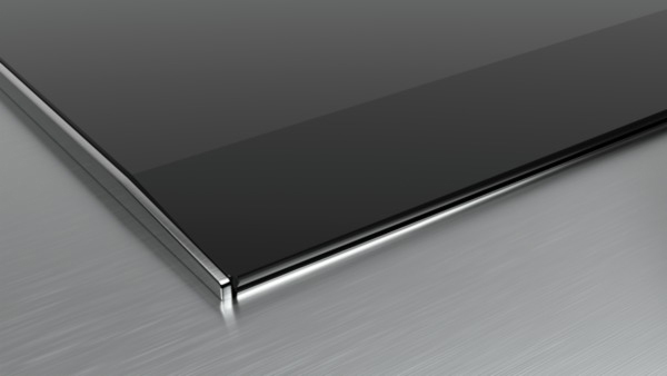 Nahaufnahme einer schwarzen Glasoberfläche mit silbernem Rand, Licht reflektiert auf metallischer Oberfläche.