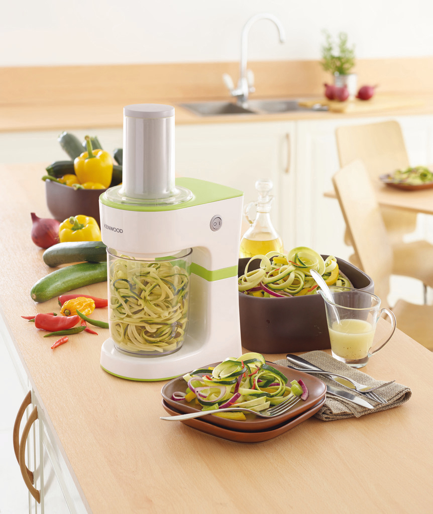 Küchentheke mit Küchenmaschine, Gemüse und einem Teller mit zubereitetem Essen.