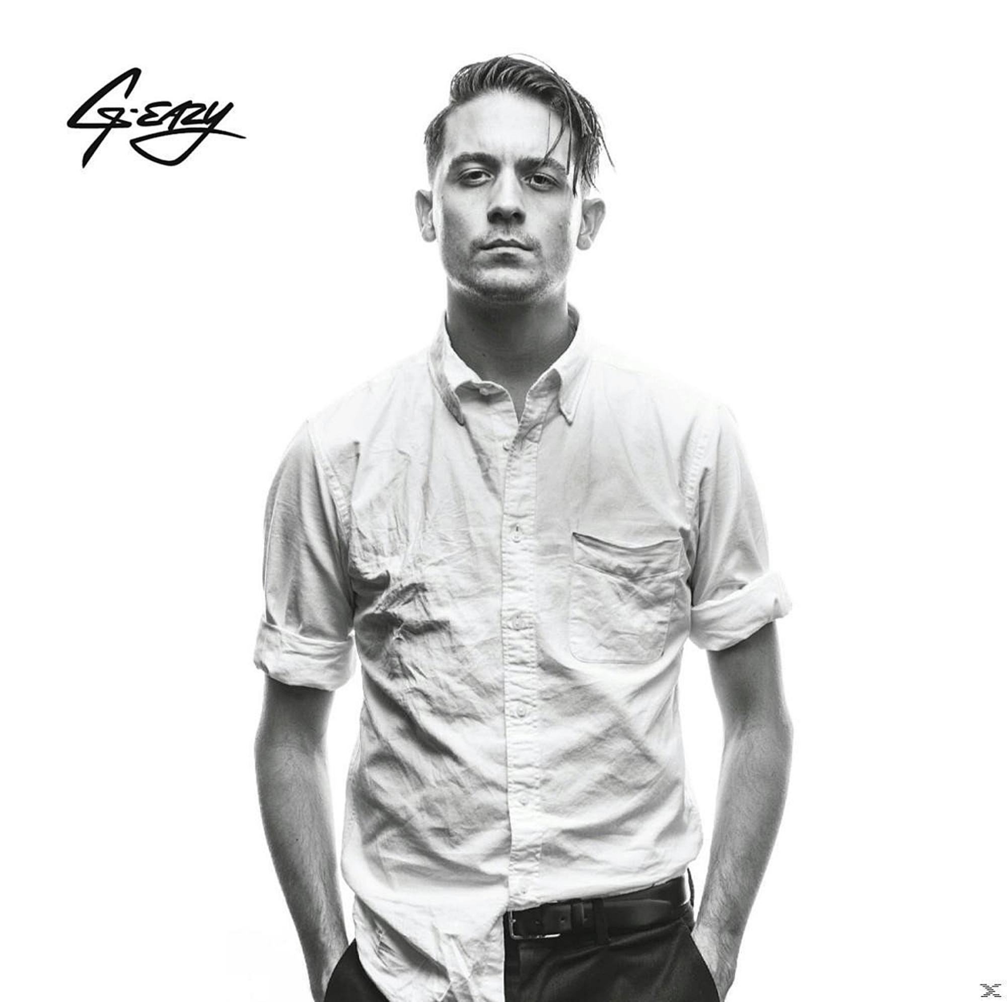 Schwarz-Weiß-Porträt von G-Eazy. Er trägt ein weißes Hemd, Hände in den Taschen, blickt den Betrachter an.