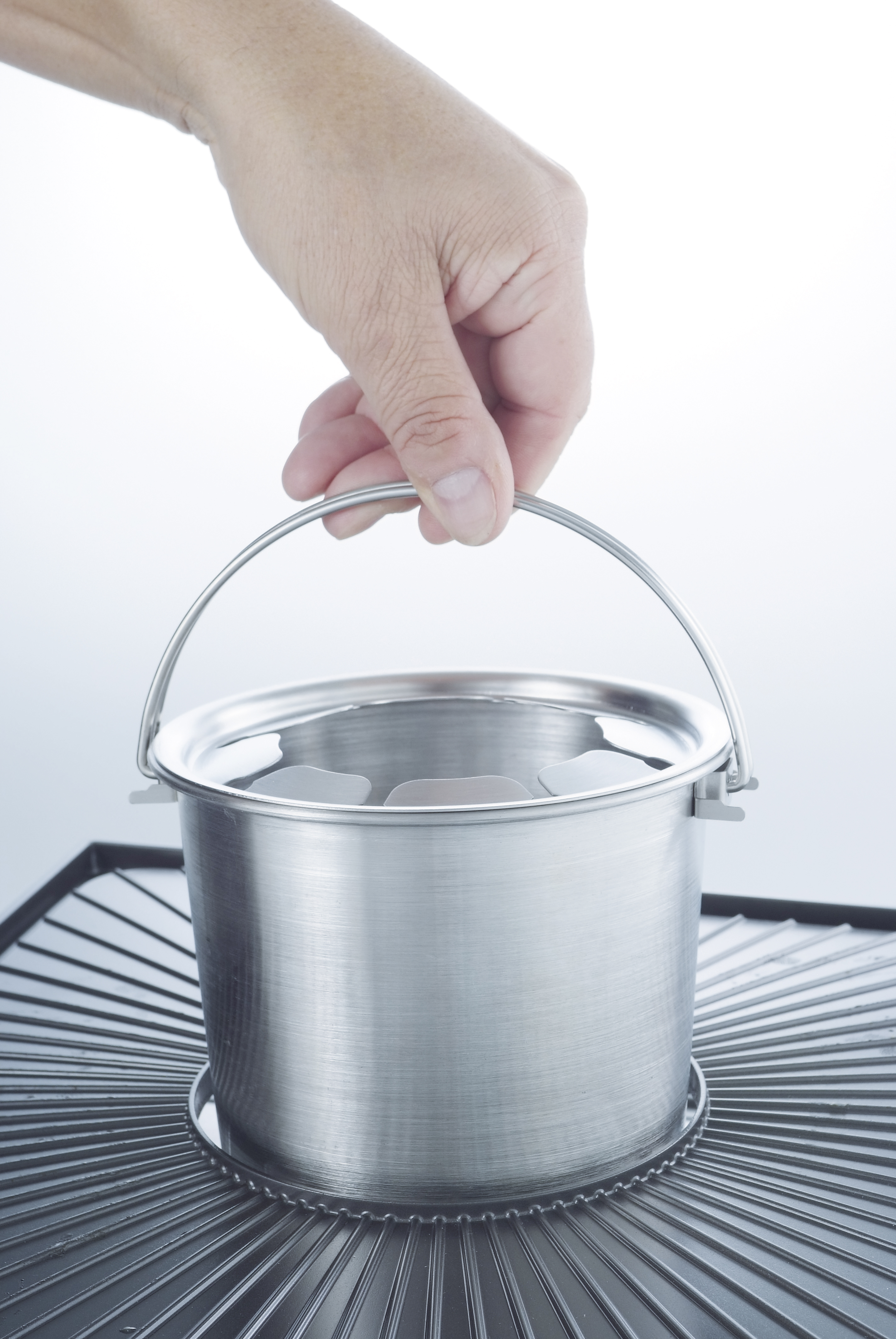 Silver bucket on a grill. A hand holds the handle above. White background.