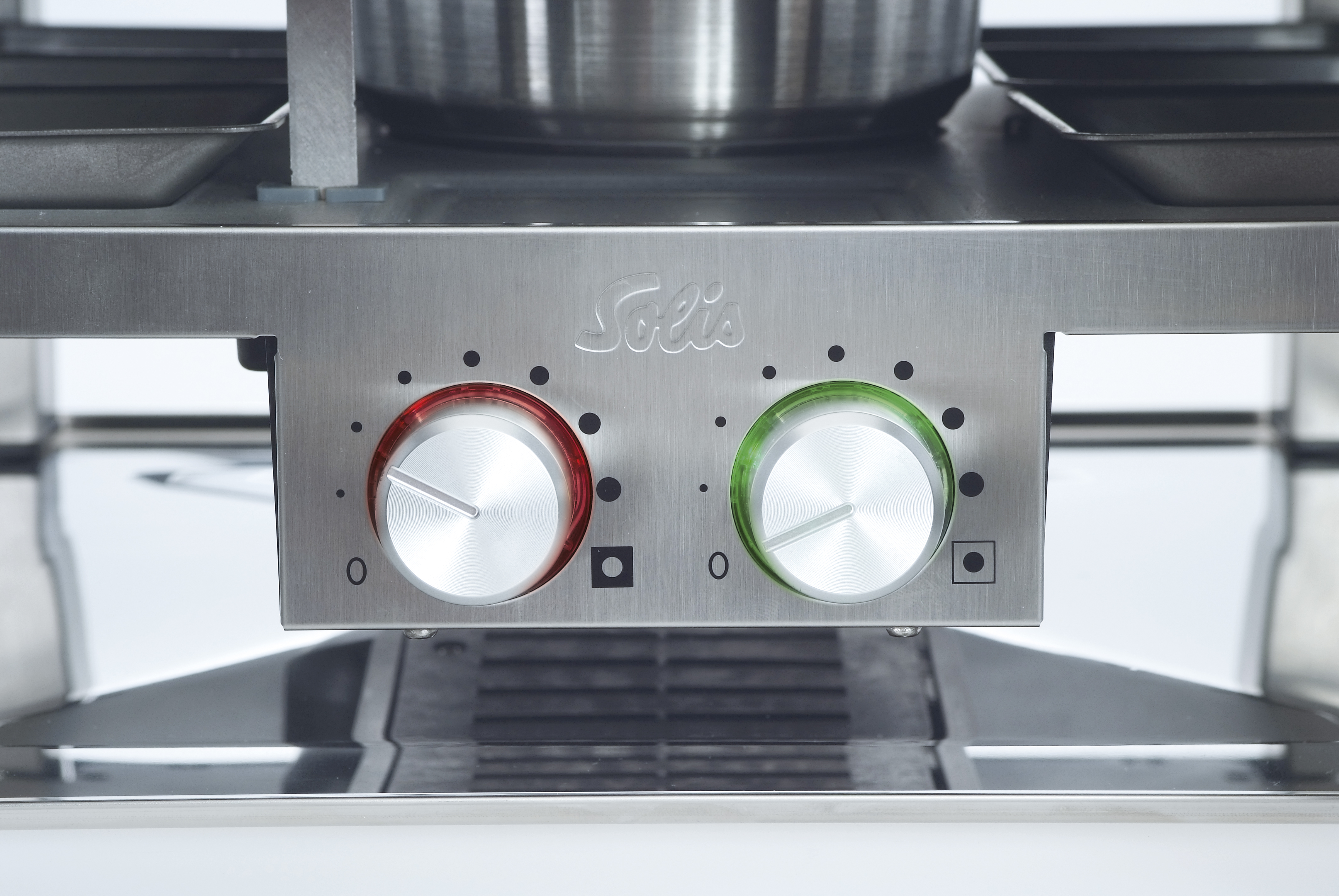 Close-up of a stainless steel appliance control panel with two red and green knobs. Silver color.