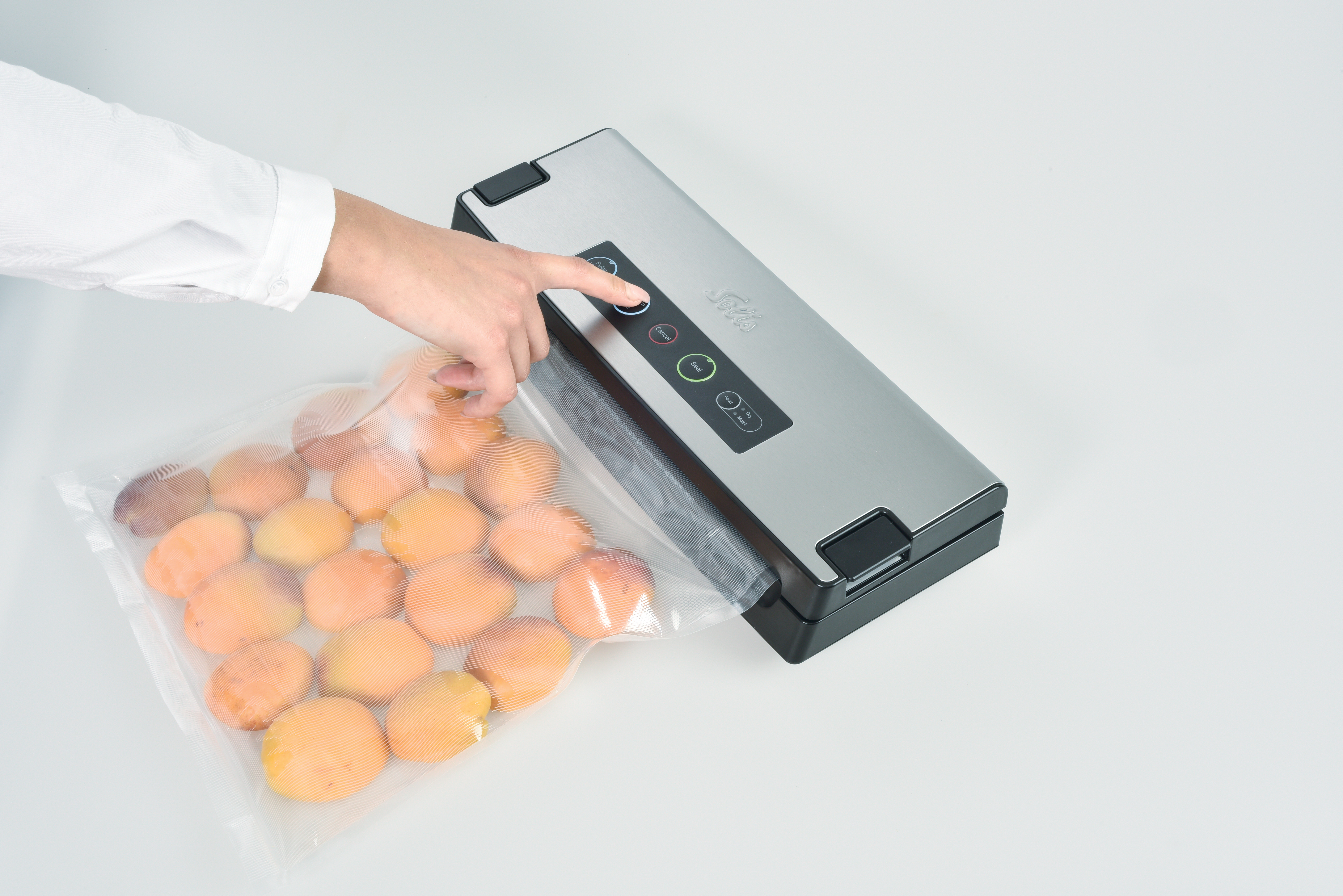 A person seals apricots in a vacuum bag with a silver and black vacuum sealer on a white surface.