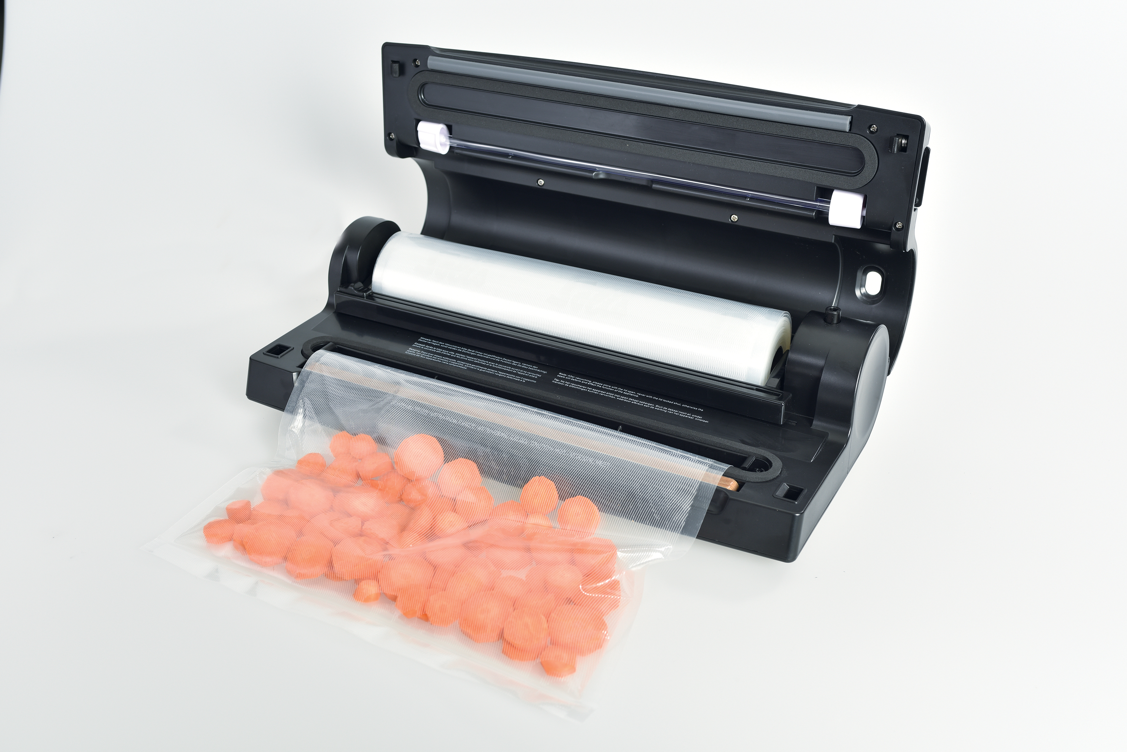 Een zwarte vacuüm sealer houdt een rol plastic vast. Een zakje oranje wortelschijfjes staat ervoor.