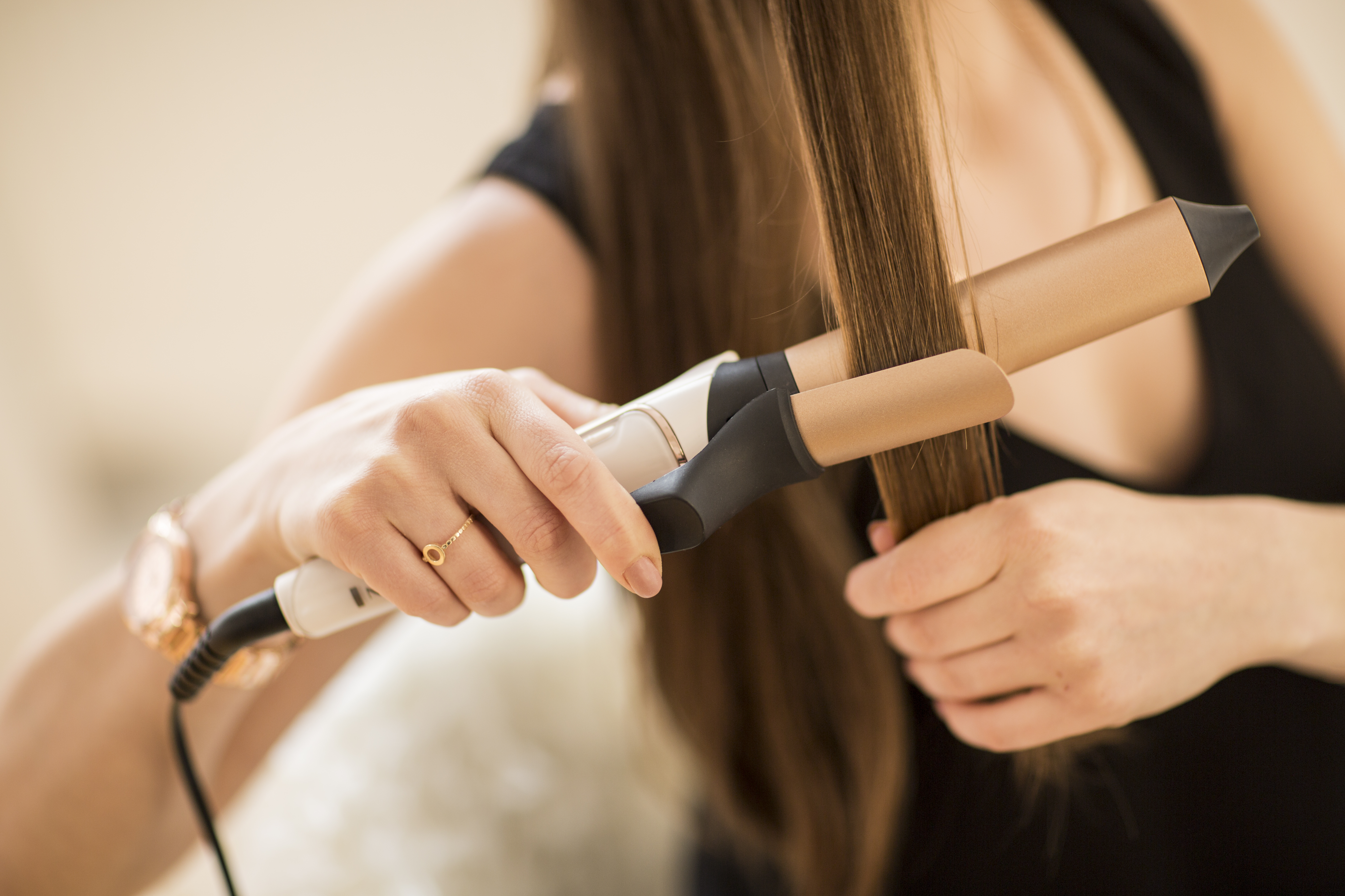 Eine Person, die ein Lockenstab hält, um Haare zu glätten. Konzentriert sich auf das Haar und das Bügeleisen.