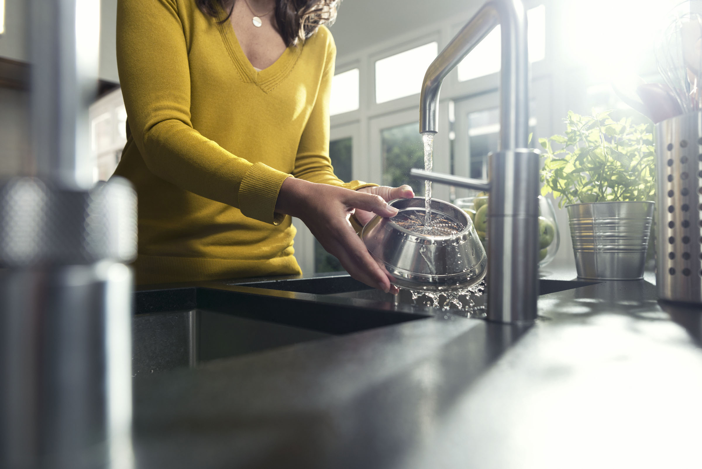 Frau wäscht eine Schüssel unter einem Küchenwasserhahn, mit natürlichem Licht.