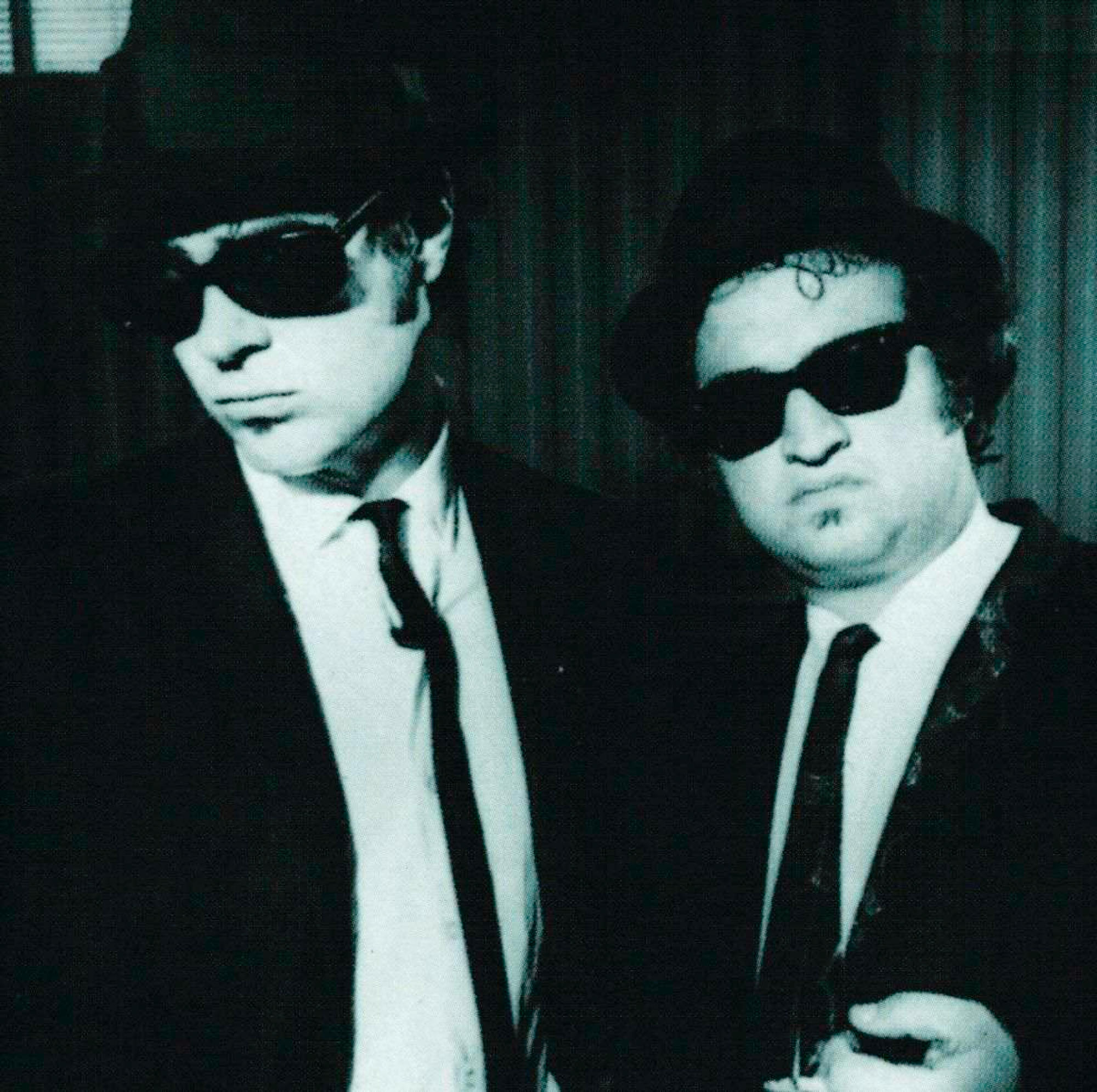 Zwei Männer in Anzügen und Hüten, Sonnenbrillen tragend. Schwarz-Weiß-Foto, die Blues Brothers.