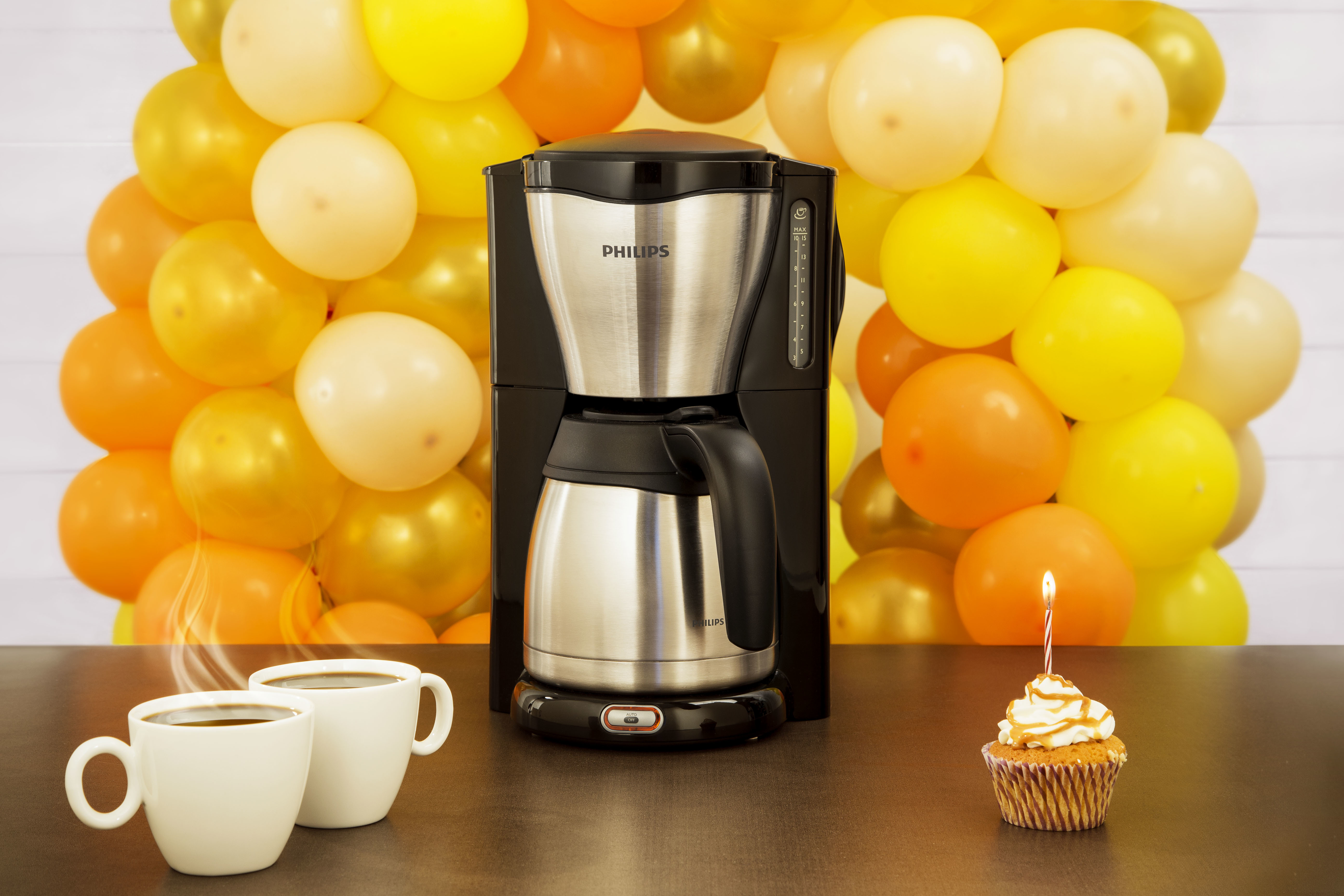 Philips Kaffeemaschine, Tassen und ein Cupcake vor gelben Ballons.