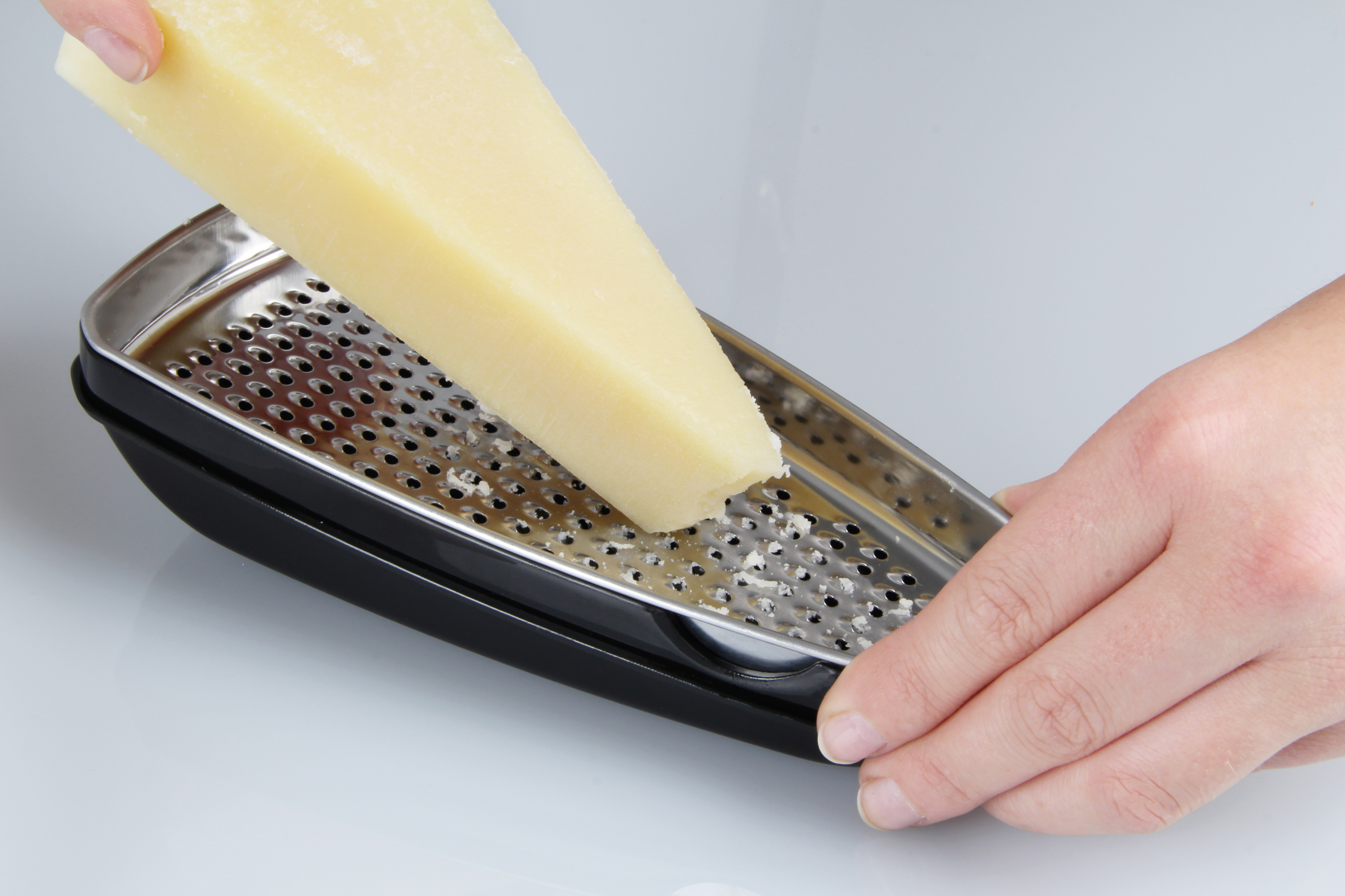 Eine Hand reibt ein großes Stück gelben Käse auf einer schwarz-silbernen Reibe.