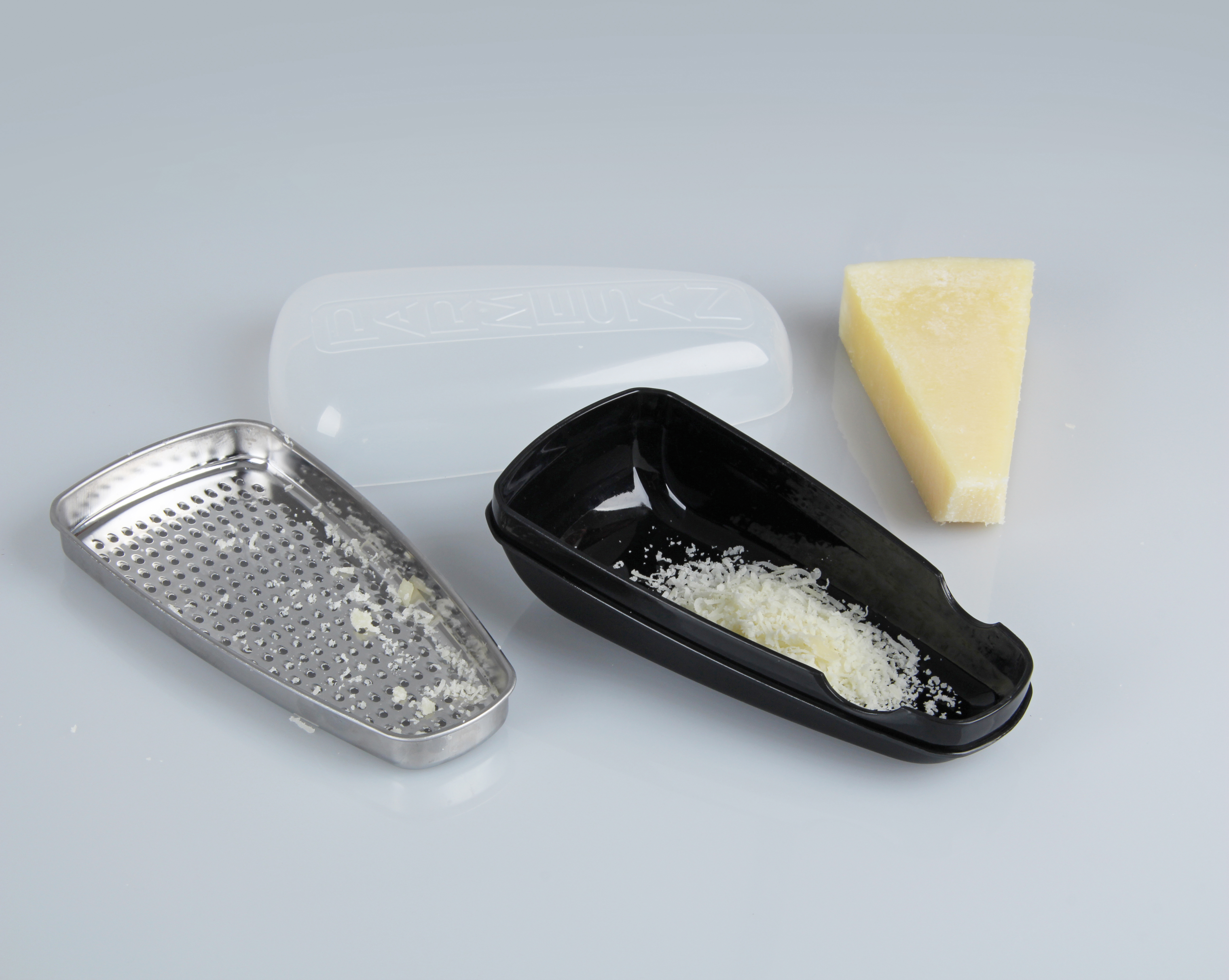 Käsereibe mit Käse und einem Stück Käse, weißer Hintergrund.