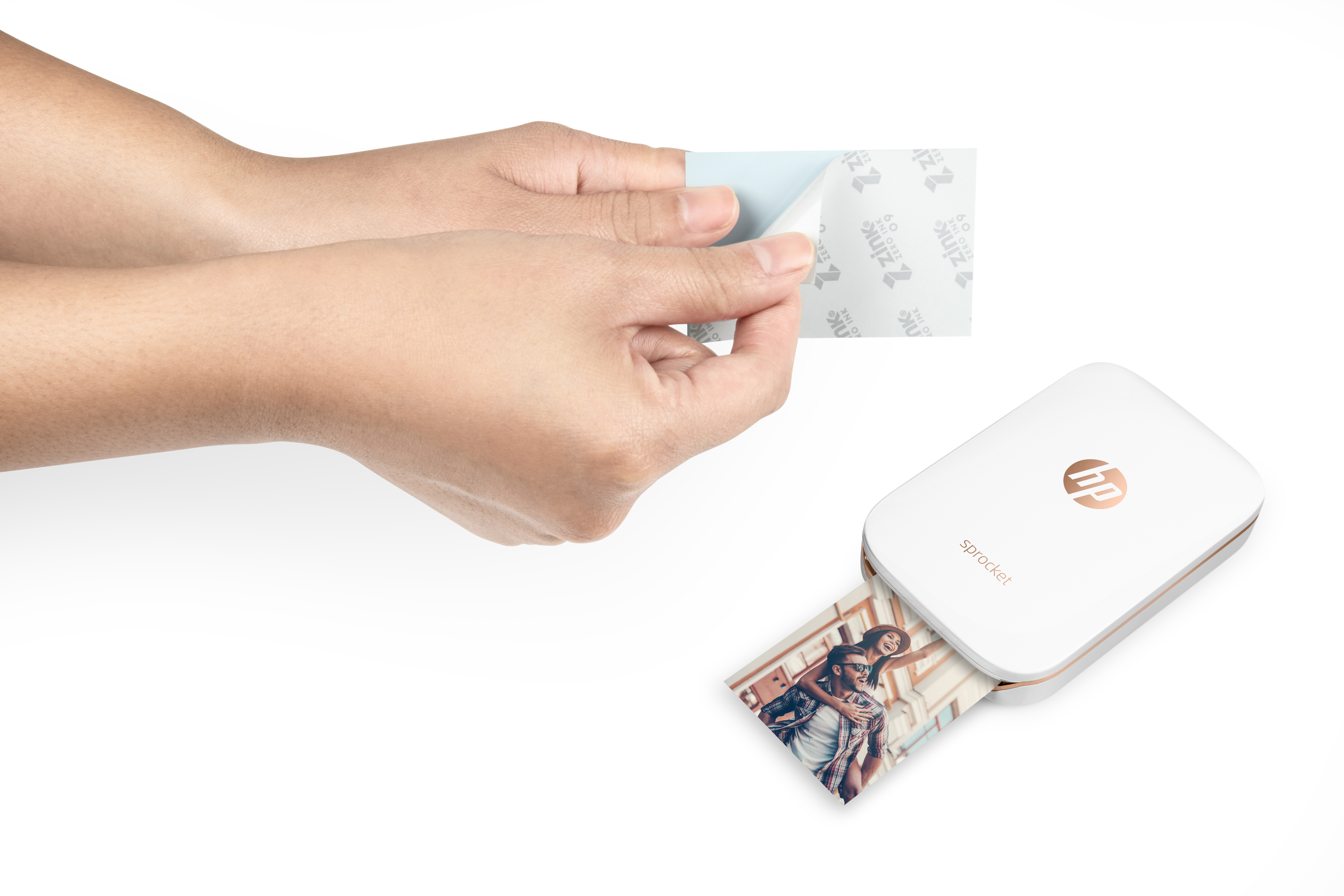 Hände, die eine Schutzfolie von einem Foto abziehen. Rechts ein weißer HP Sprocket Drucker.