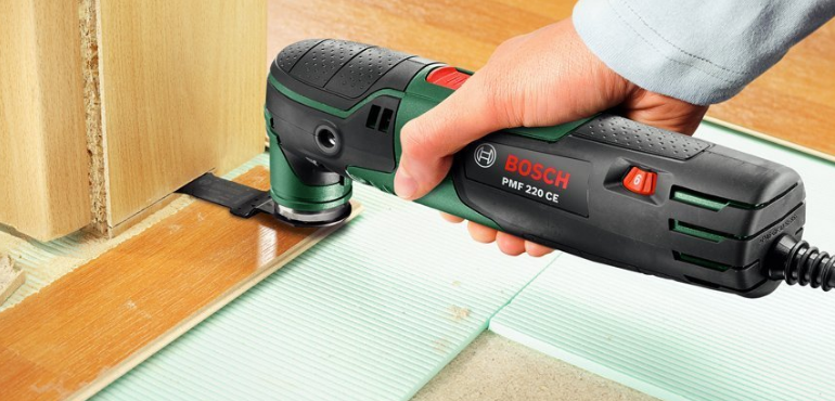 Egy kéz, ami egy Bosch PMF 220 CE multi-szerszámot tart, ami egy fa padlót vág.