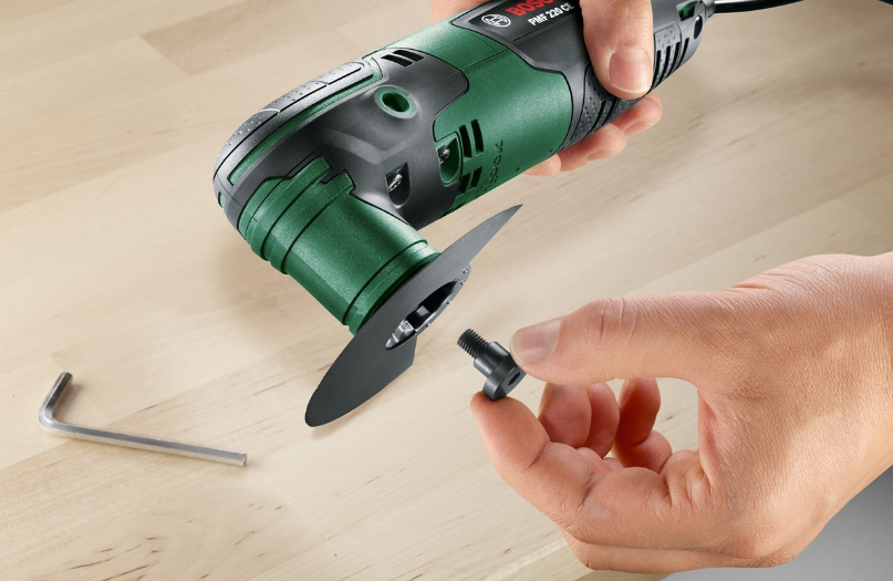 Egy zöld-fekete multitool, egy kéz eltávolítja a pengét, fa felületen.