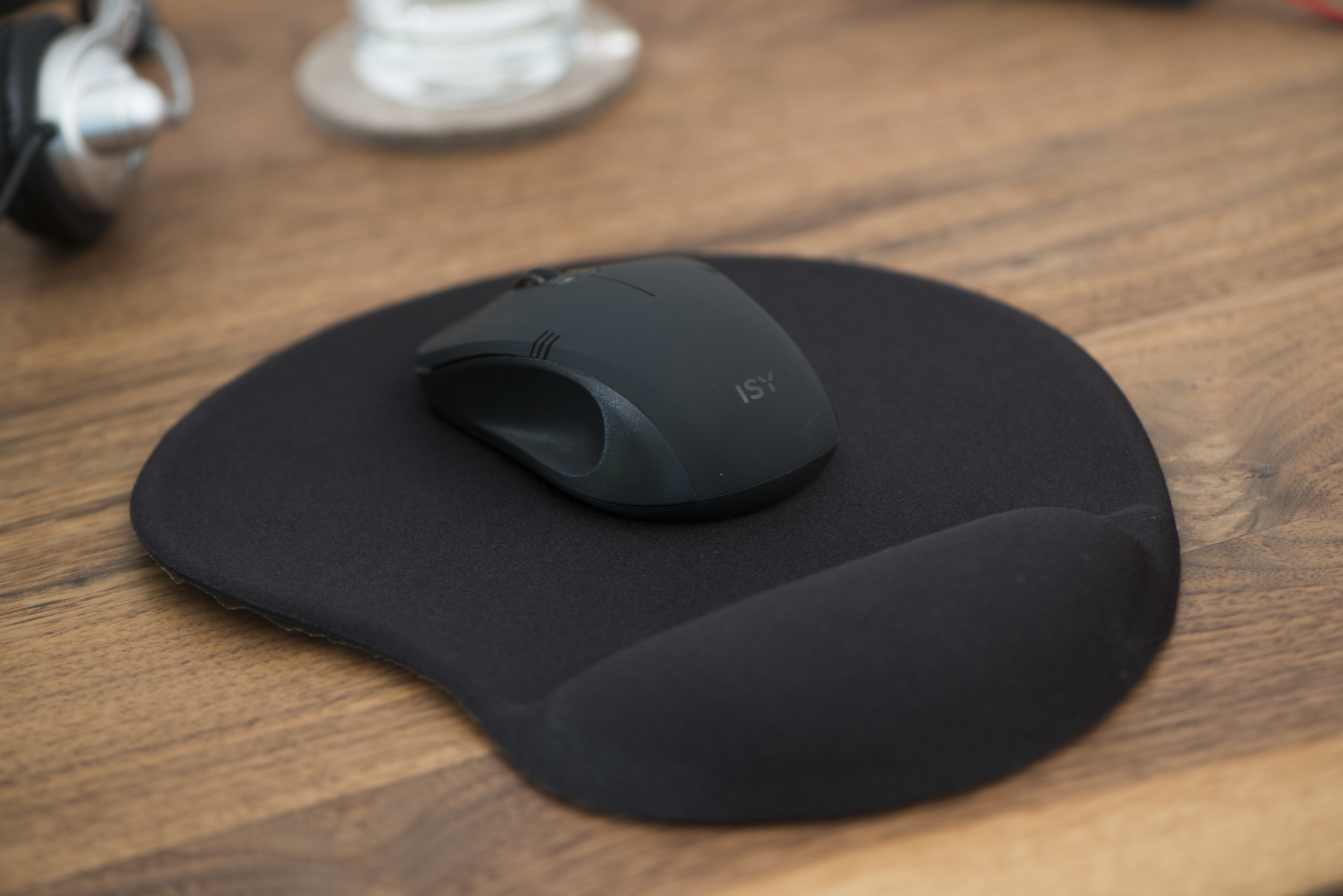 Une souris noire sur un tapis de souris noir. Ils sont sur un bureau en bois. Arrière-plan flou.