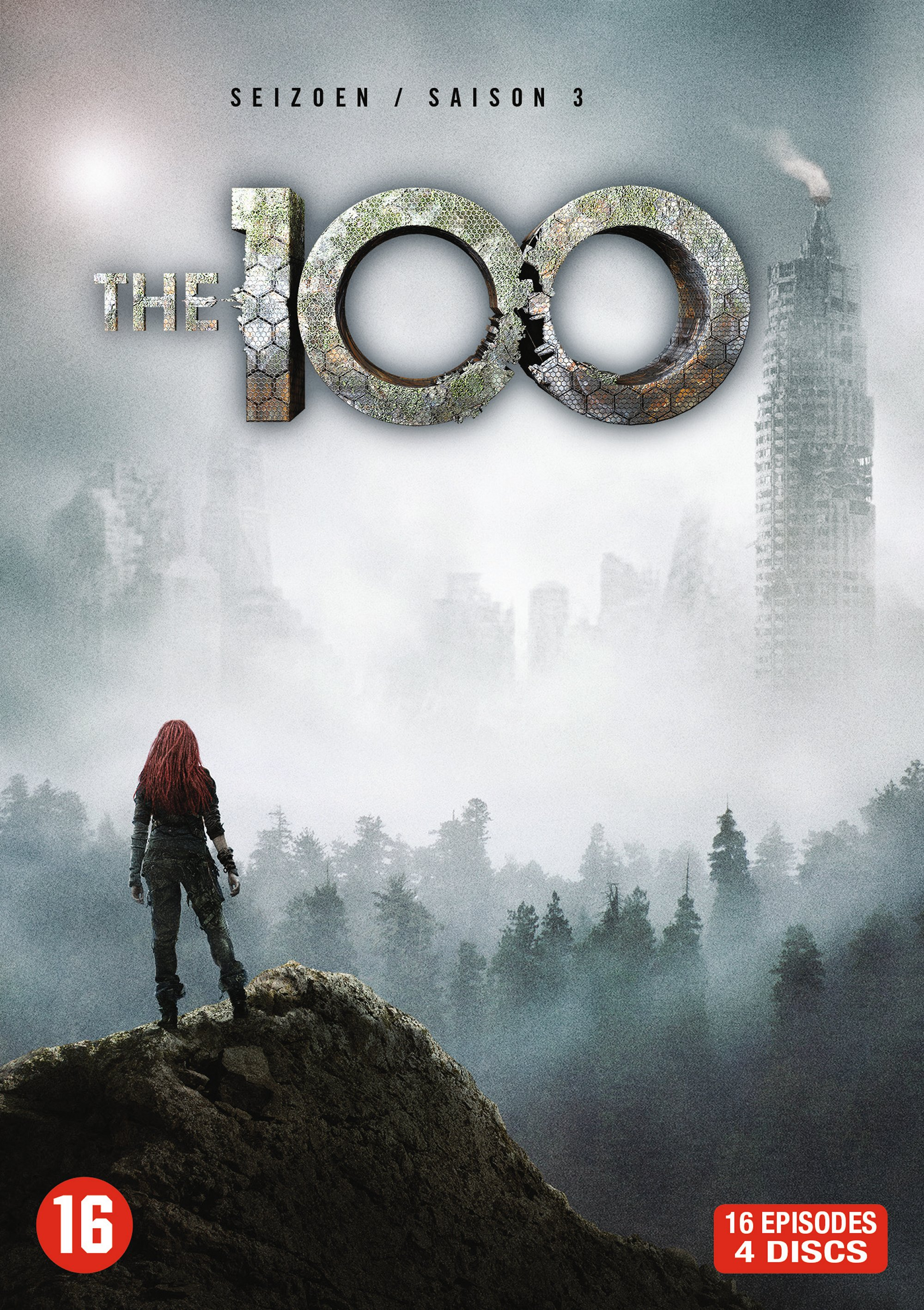 A woman with red hair stands on a rock in front of a misty cityscape.