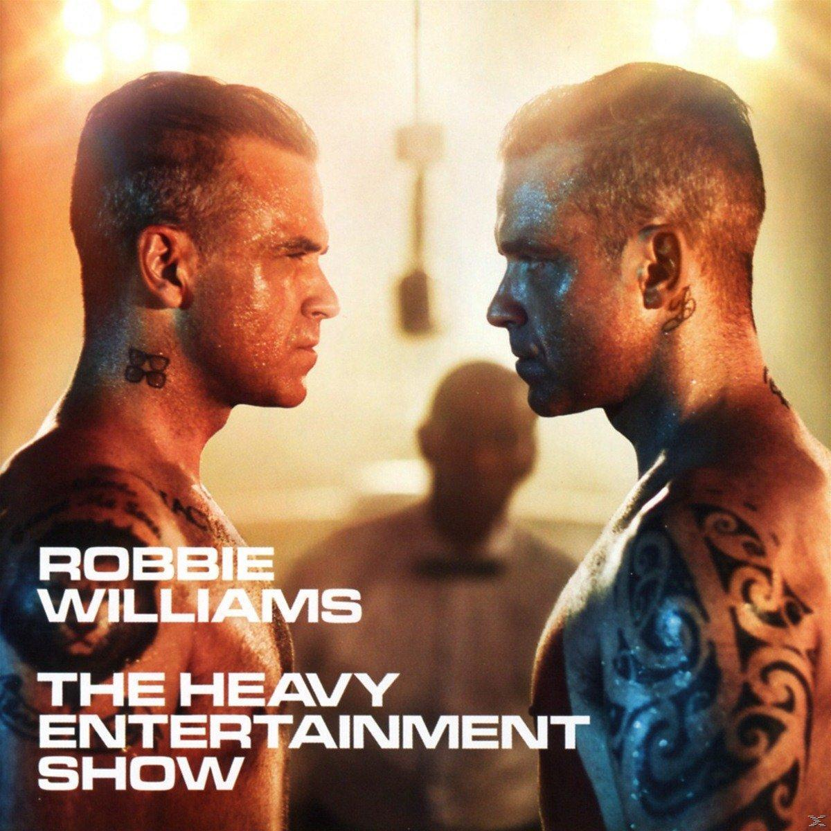 Deux hommes se font face, Robbie Williams et un autre, tatouages visibles. Le titre 'The Heavy Entertainment Show' est affiché.