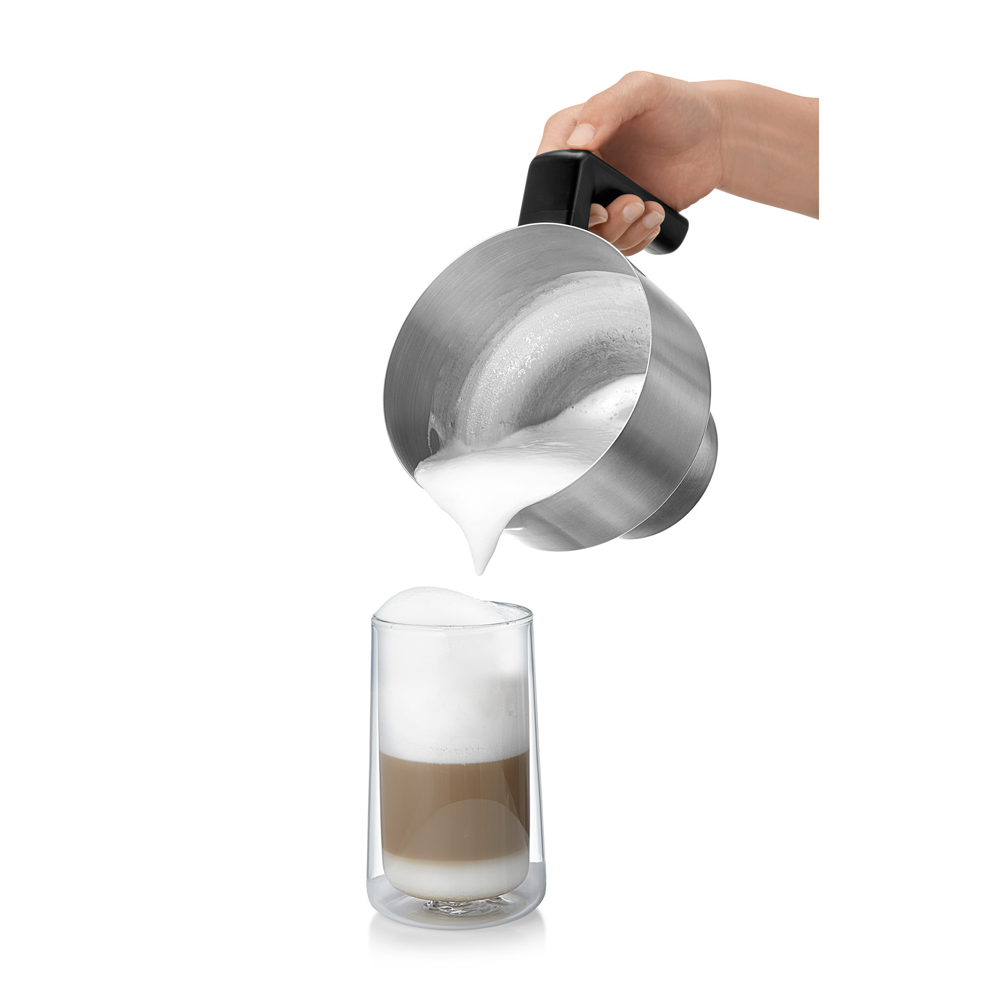 Hand gießt geschäumte Milch aus einem Edelstahlkrug in ein Glas Latte.