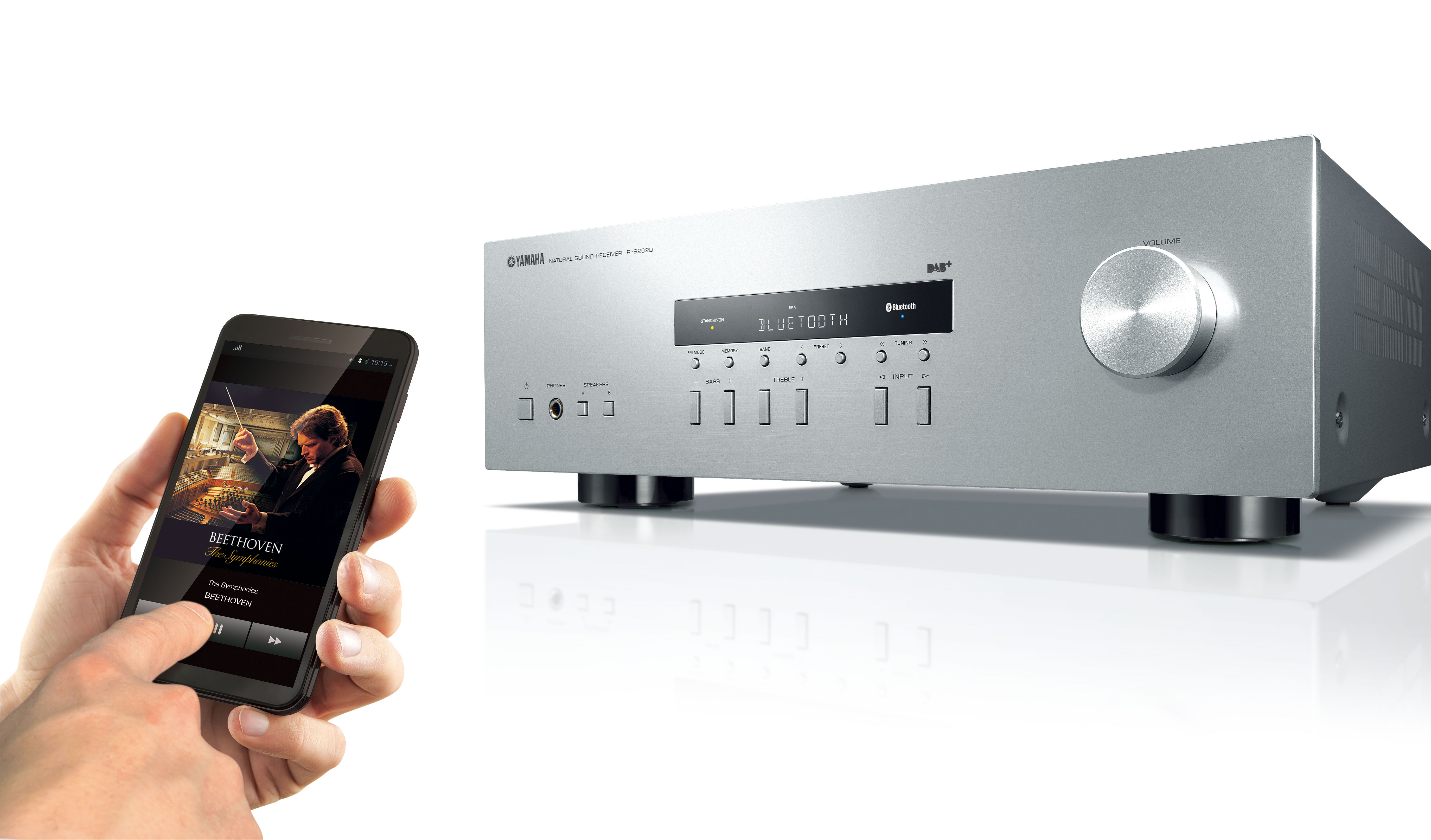 Die Hand einer Person berührt ein Smartphone, mit einem Stereo-Receiver und einem Musikplayer im Hintergrund.
